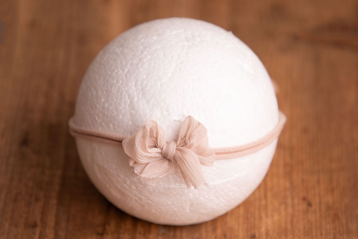 White wool felt ball with delicate blush pink chiffon bow headband on wood.