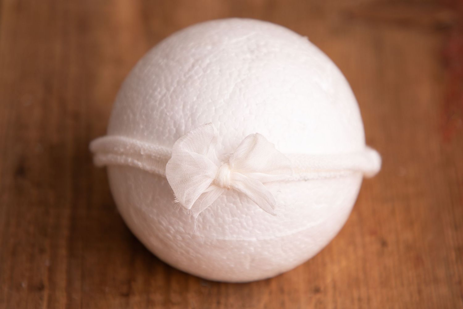 White knit ball with a delicate ivory organza bow headband on a wooden background.