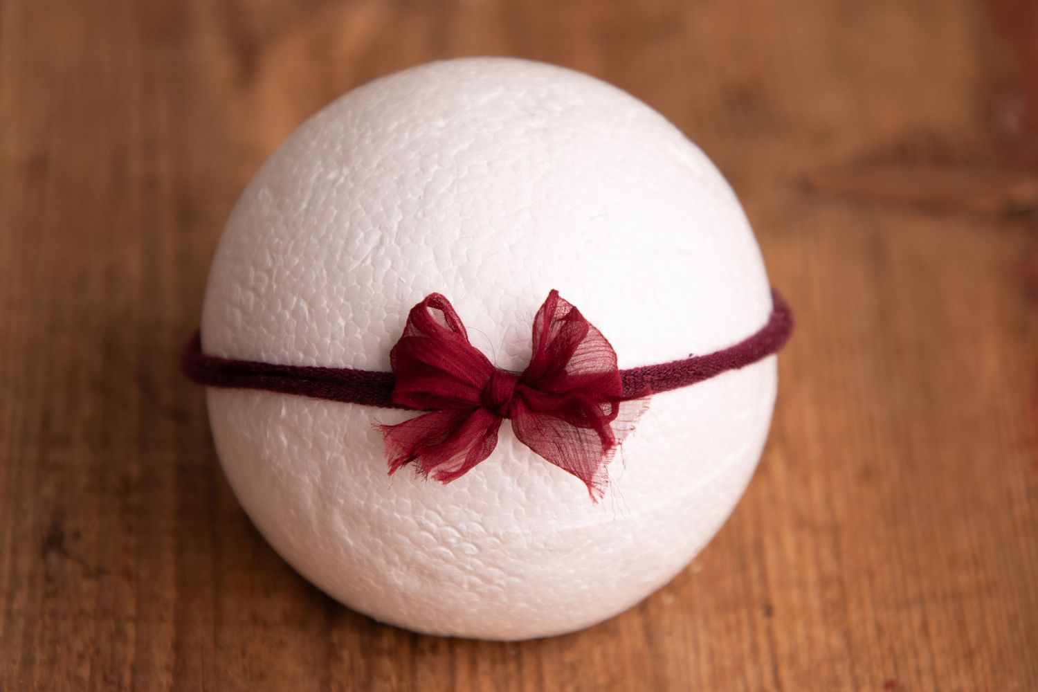 White wool felt ball with deep red organza bow on burgundy elastic headband.
