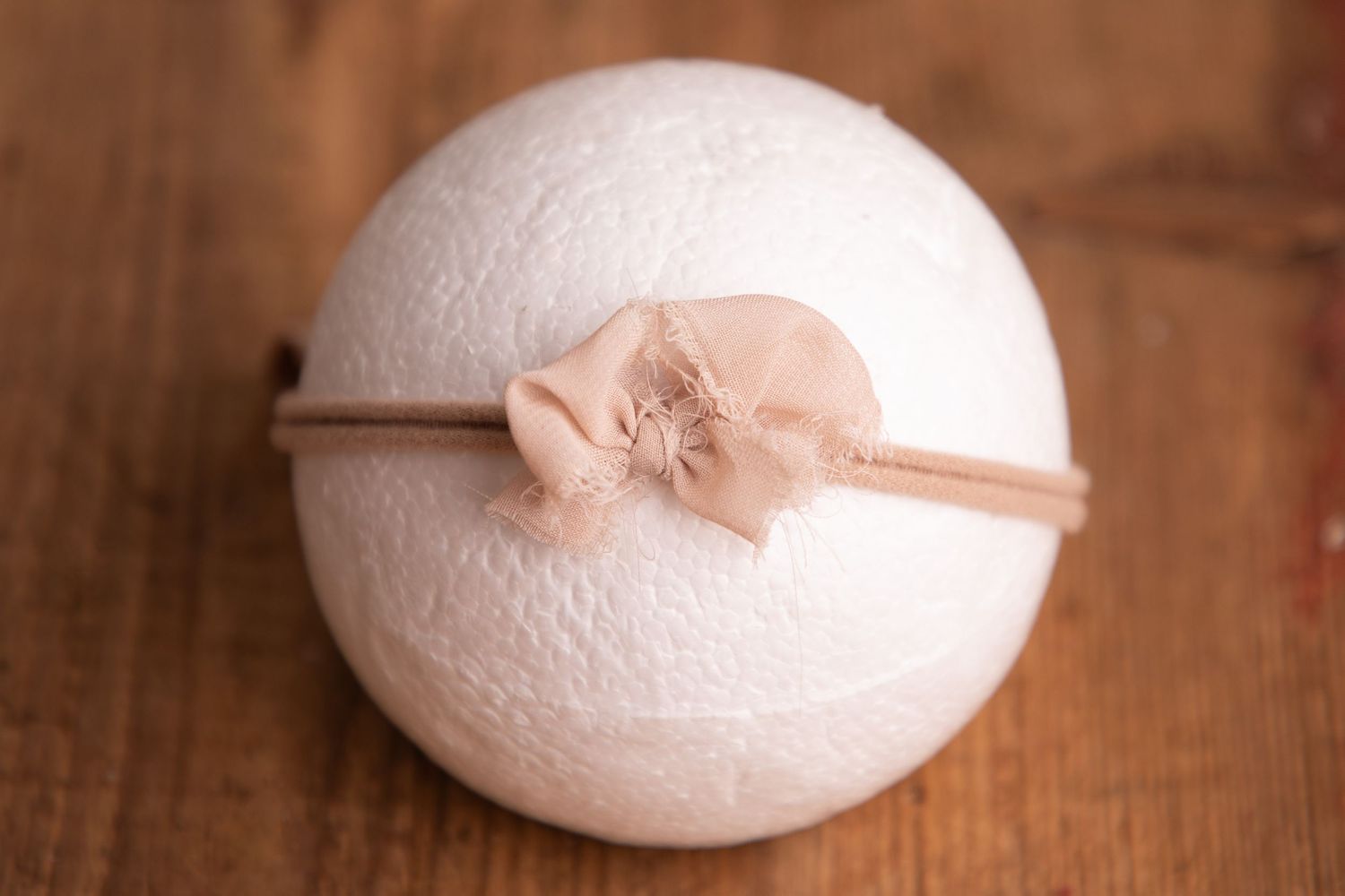 White knit ball with a sheer blush chiffon bow headband on a wooden surface.