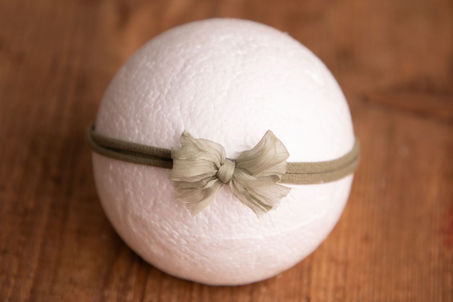 White knit ball displayed with an olive green fabric bow headband on a wooden surface.