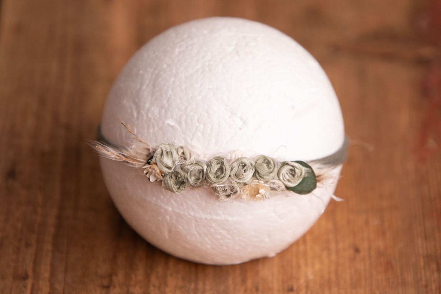 Sage green rosette headband with dried botanicals on white sphere newborn photography prop.