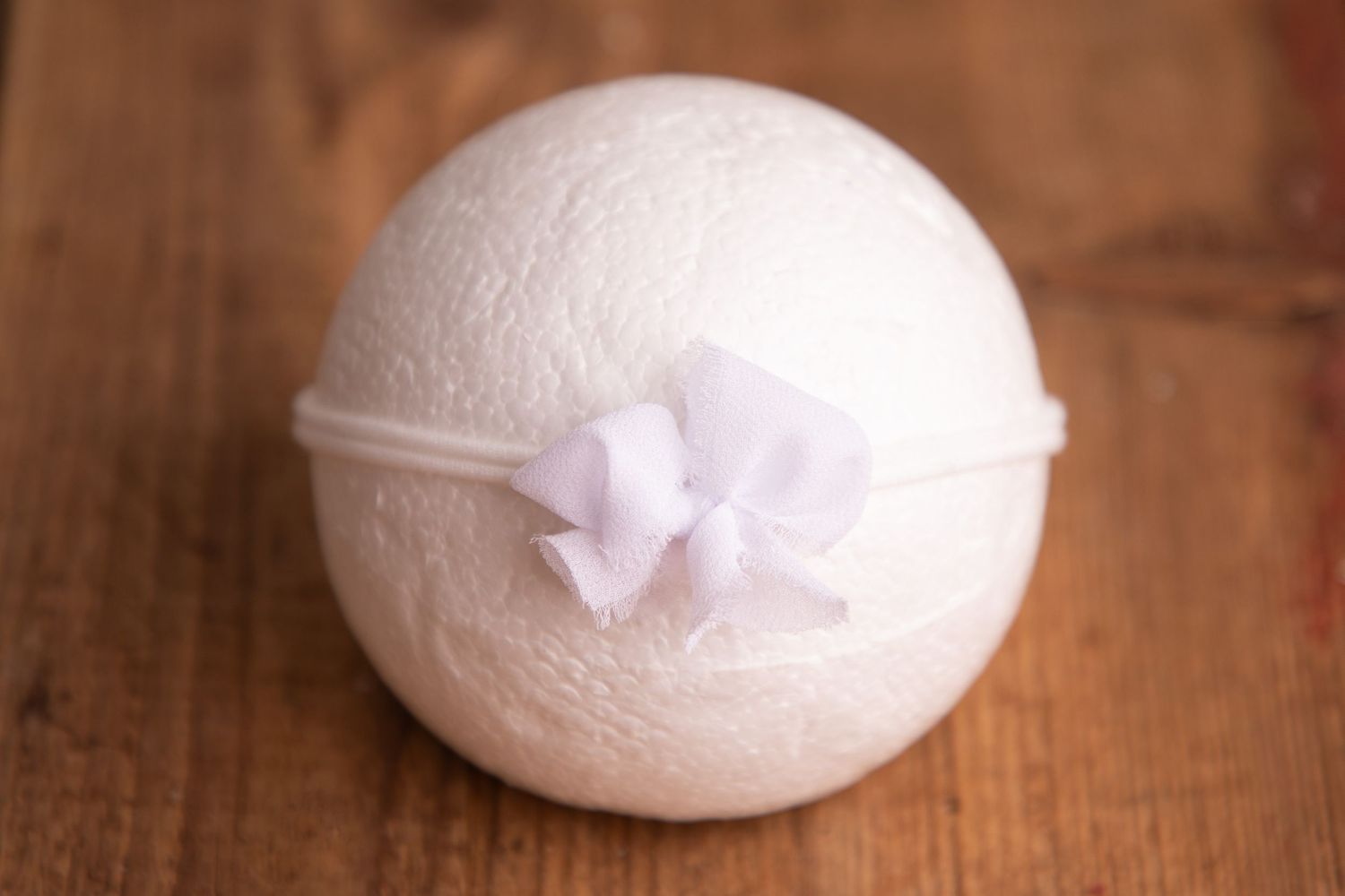 White knit ball with a delicate lavender ribbon bow headband on a wooden surface.