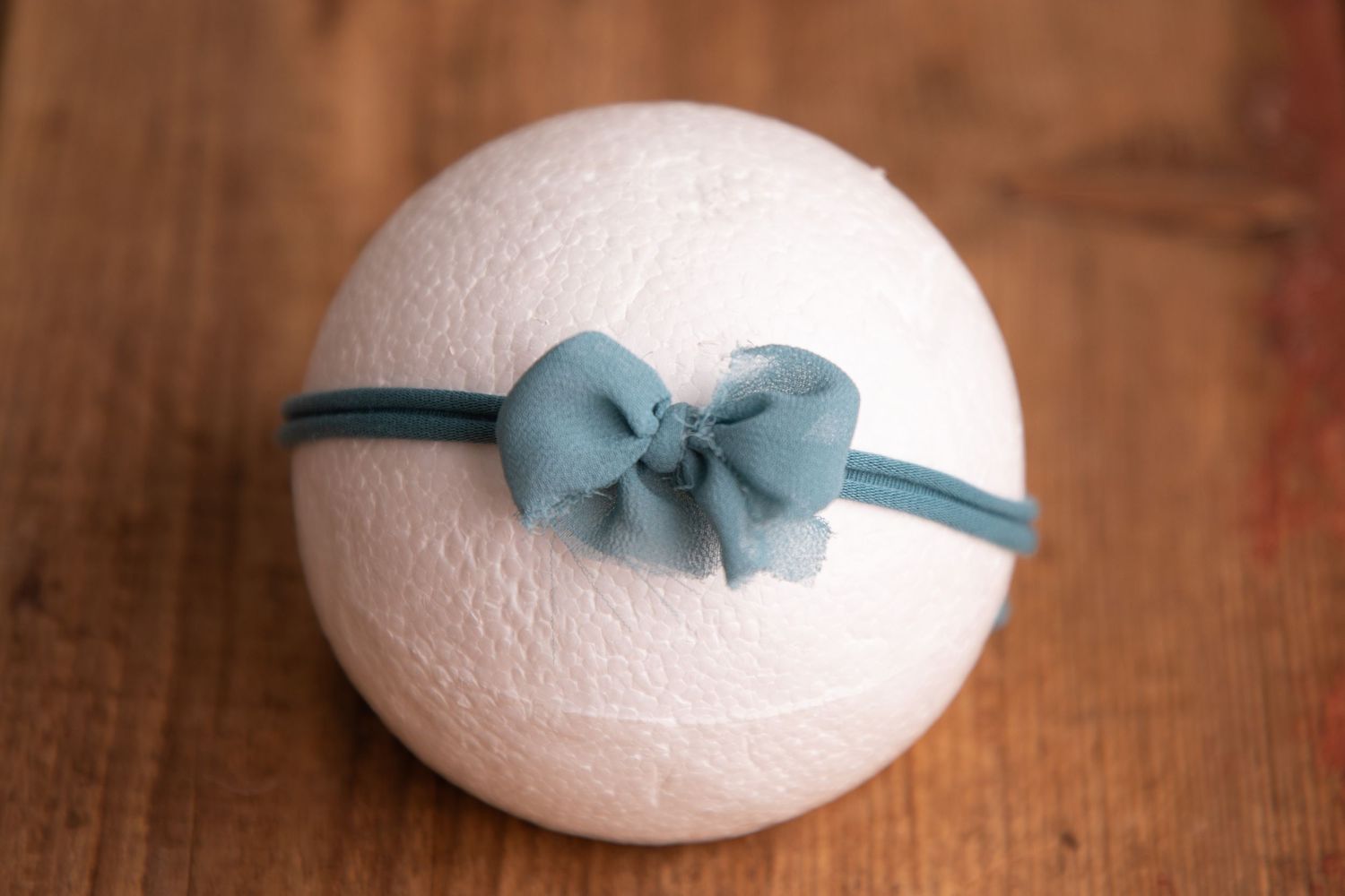 White wool felt ball with teal blue organza bow headband on wooden background.