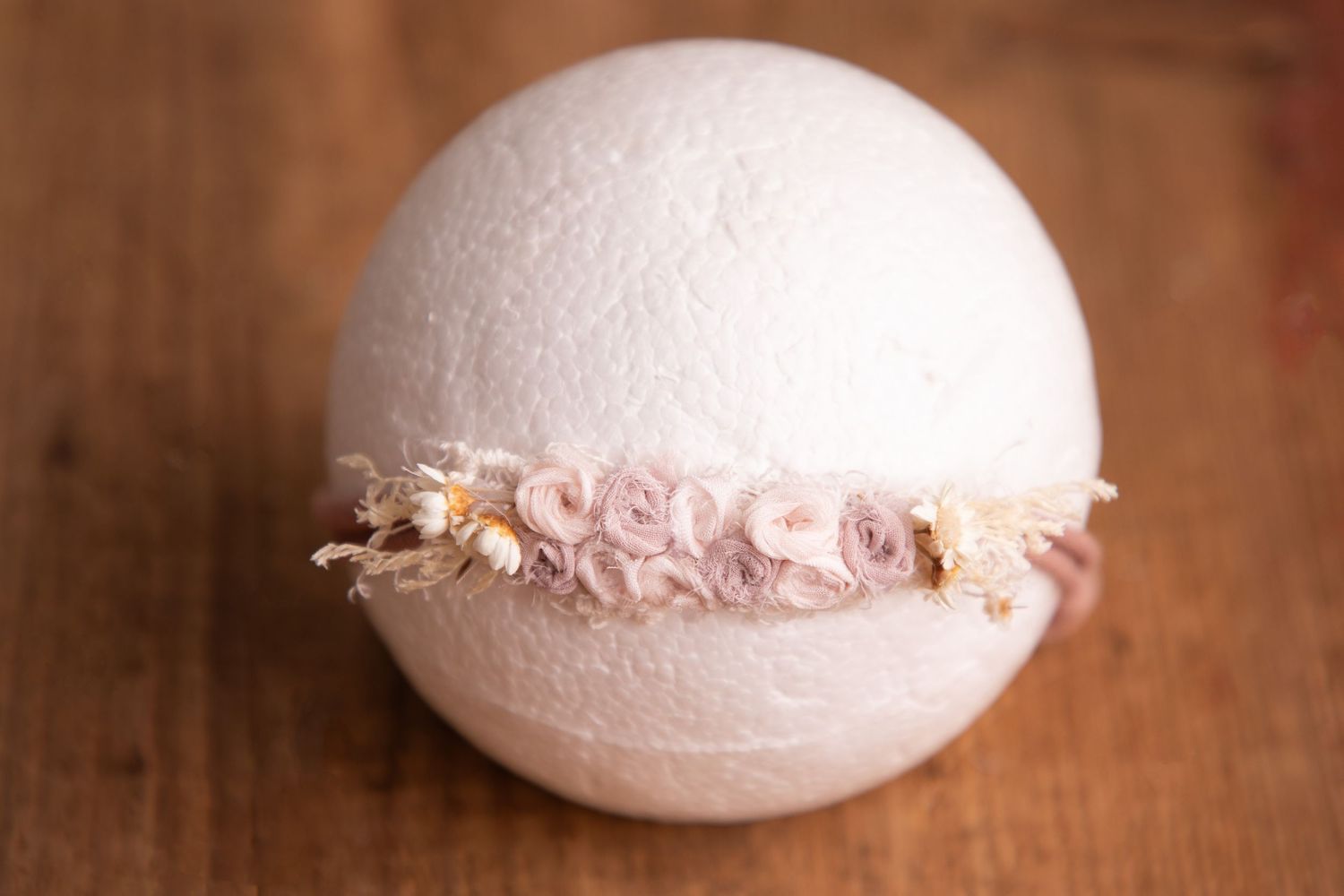 Soft pink floral headband with dried flowers on white sphere newborn photography prop.
