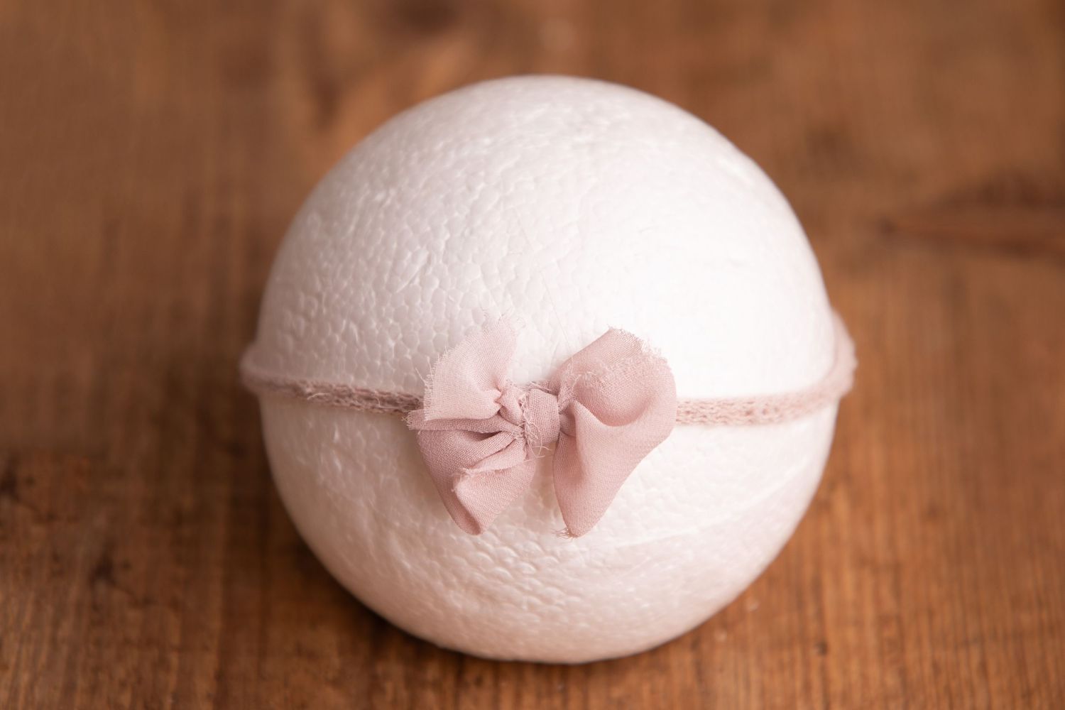 White wool felt ball with small dusty pink fabric bow on pink headband.