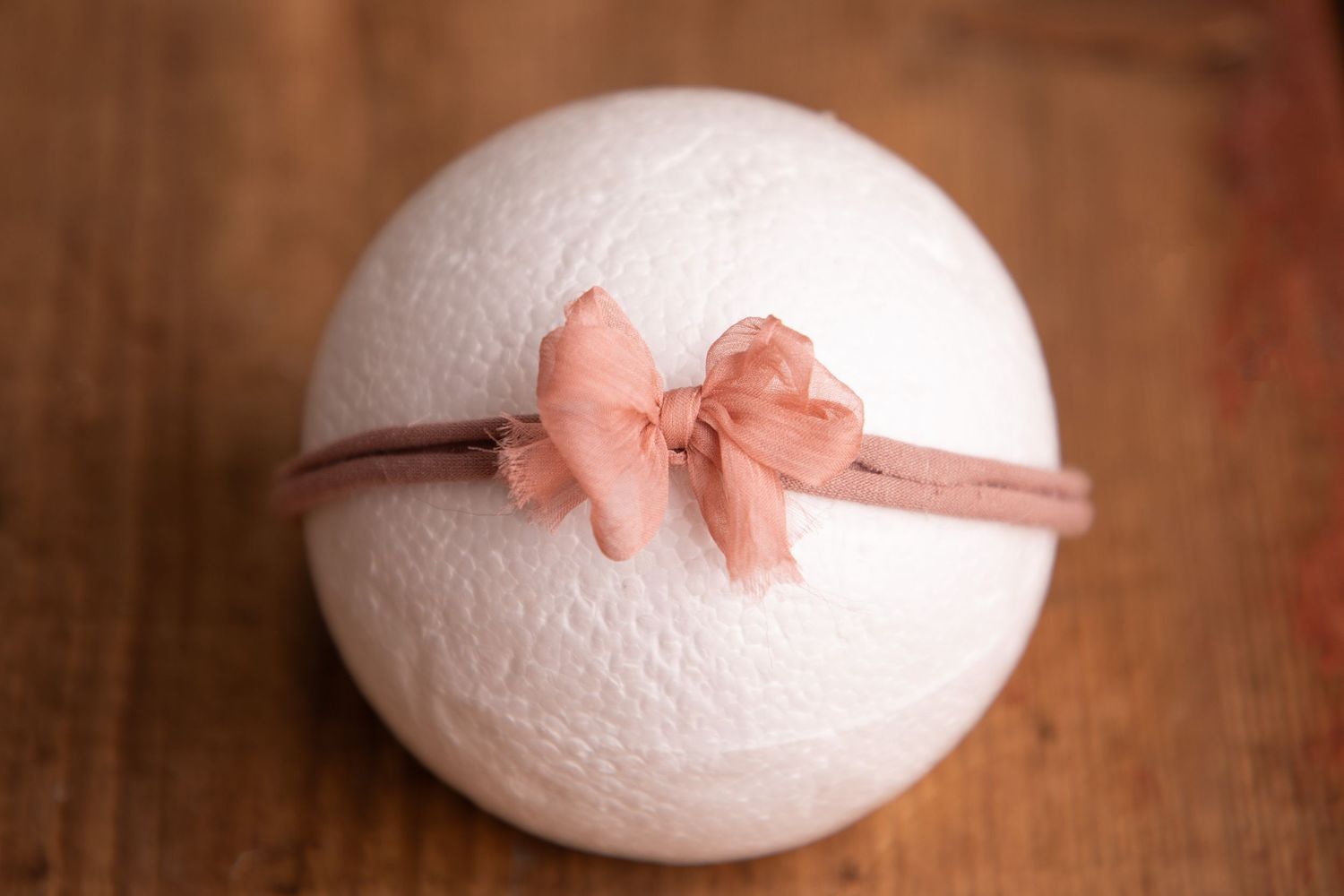 White knit ball with a coral chiffon bow headband displayed on a wooden surface.