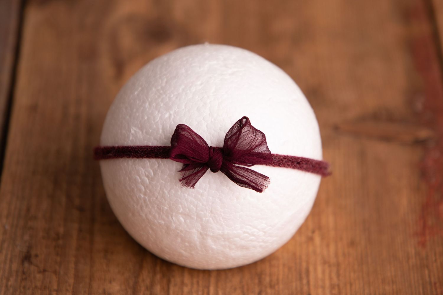 White wool felt ball with dark burgundy organza bow headband on wooden surface.