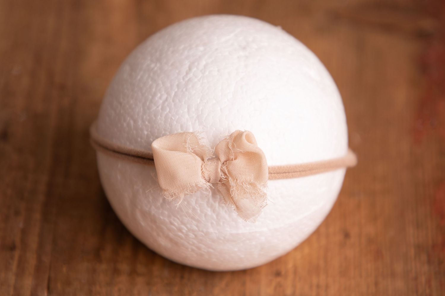 Delicate peach bow headband on white sphere newborn photography prop on wooden background.