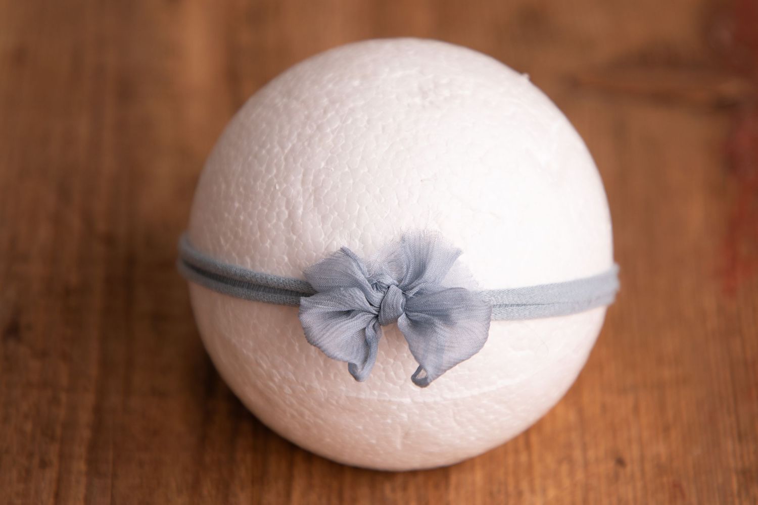 White wool felt ball with gray organza bow headband on rustic wooden surface.