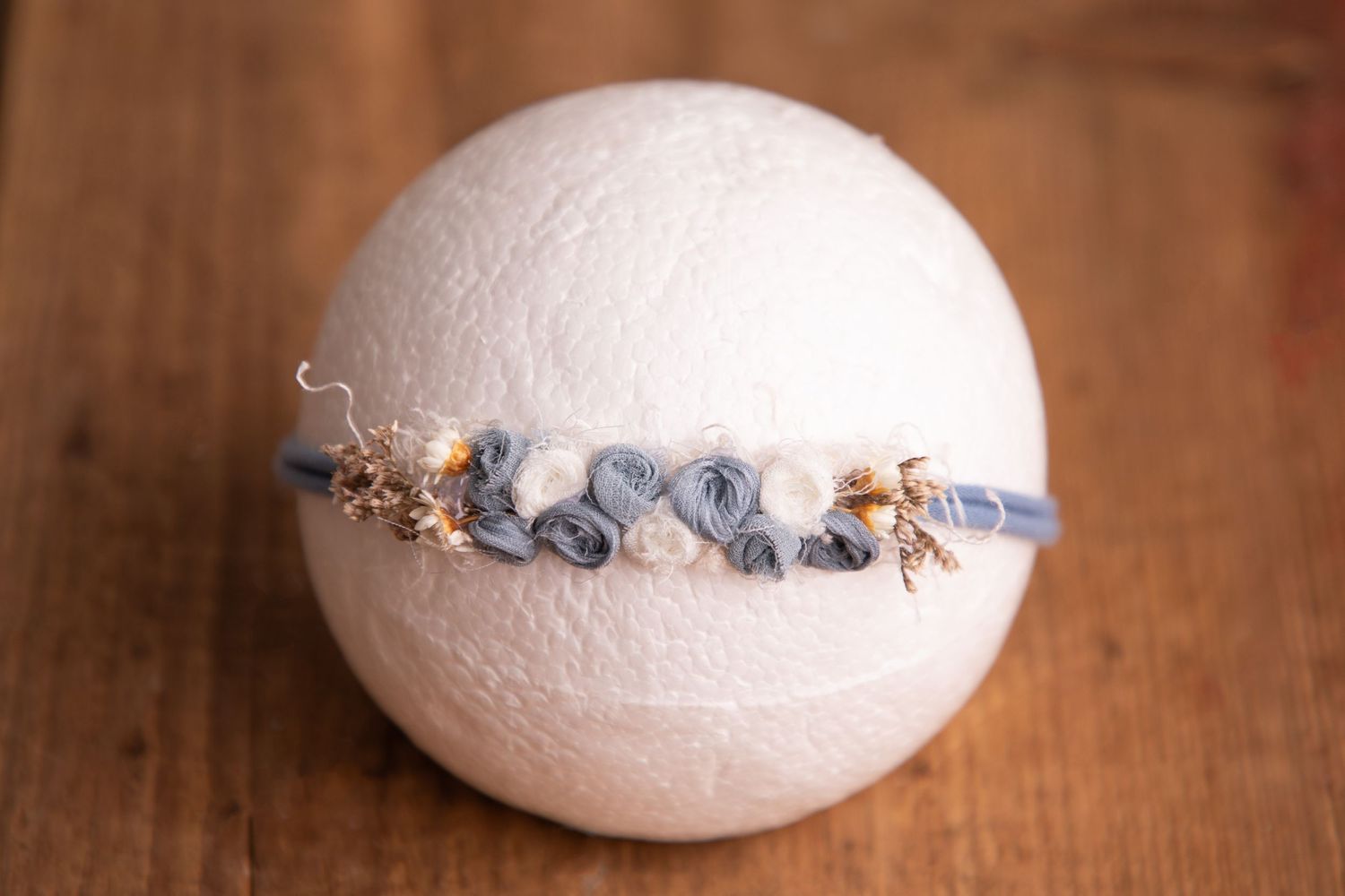 Blue rosette flower headband with gold accents on white sphere newborn photography prop.
