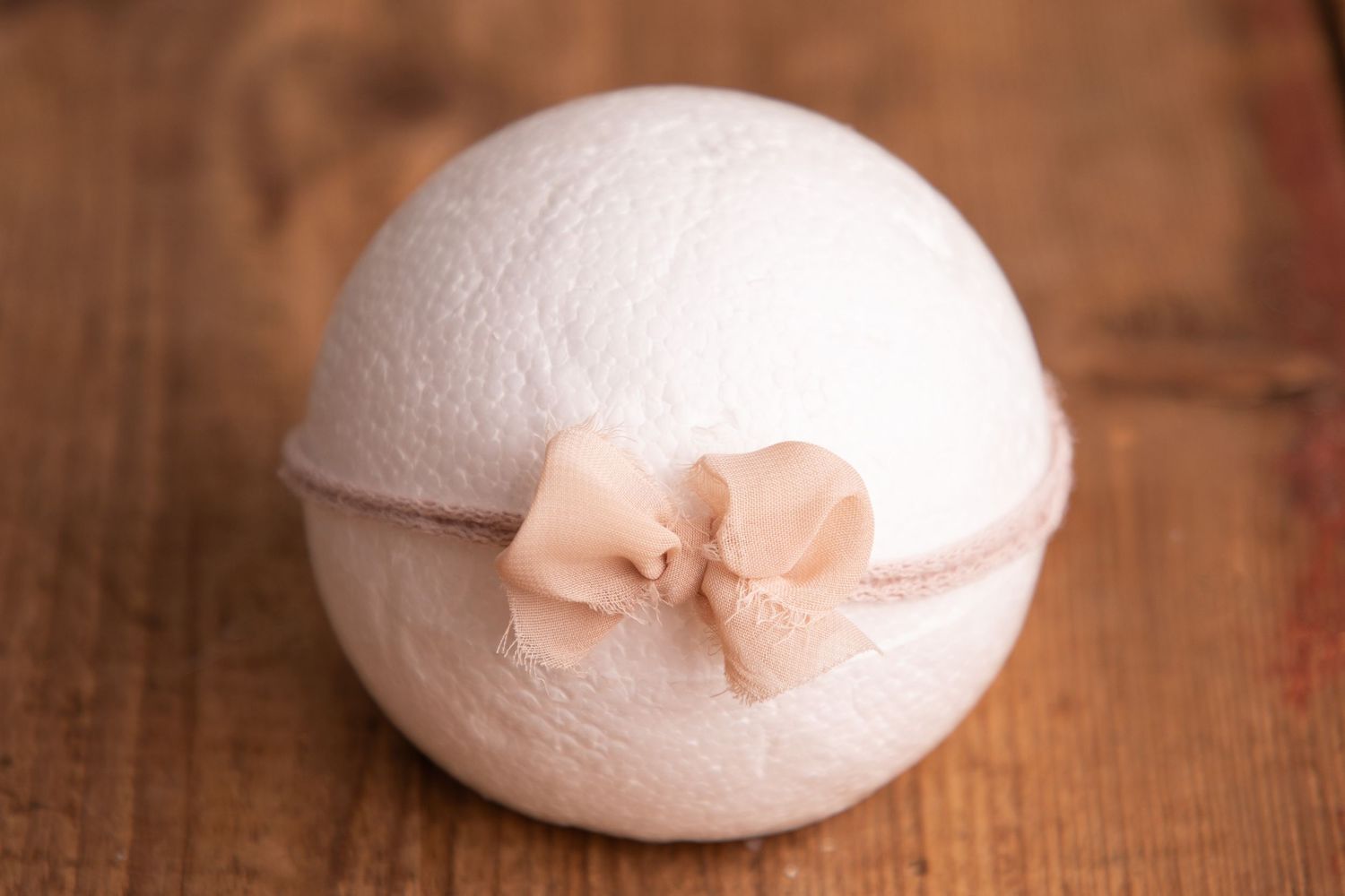 White knit ball with a soft peach ribbon bow headband on a rustic wooden background.