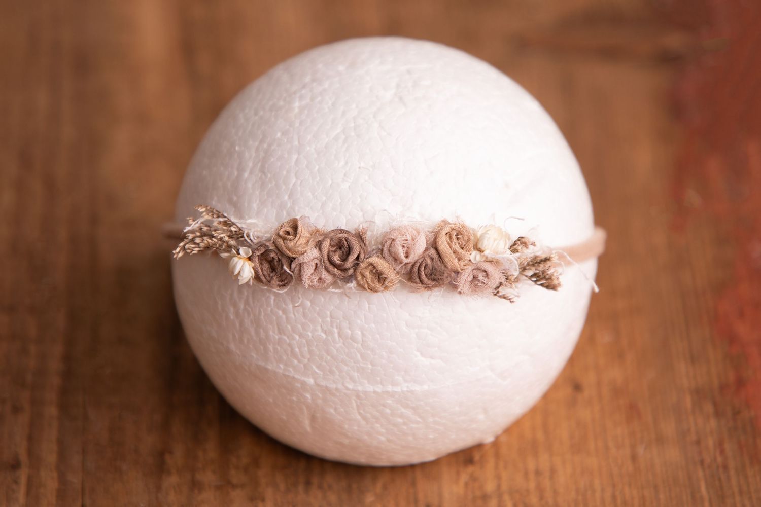 Tan rosette flower headband on white ball newborn photography prop on wooden surface.