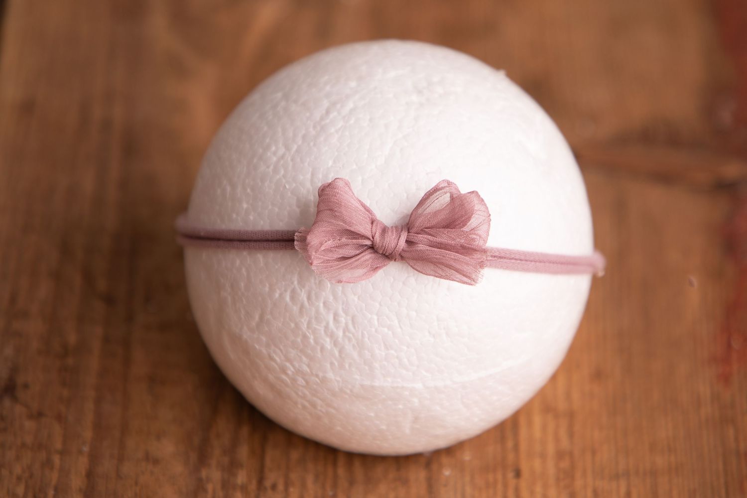 White knit ball with a dusty rose organza bow headband on a wooden background.