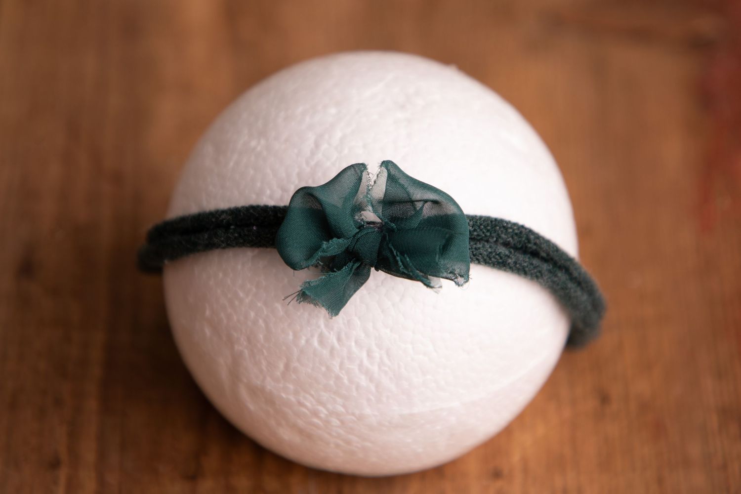 White knit ball with a dark green velvet bow headband on a wooden surface.