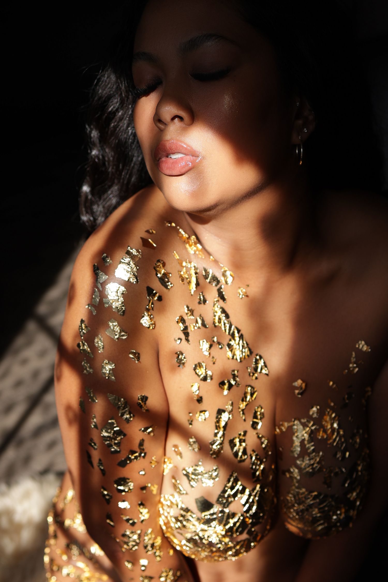 Natural light shining through a window on a woman with golden skin wearing nothing but gold flakes