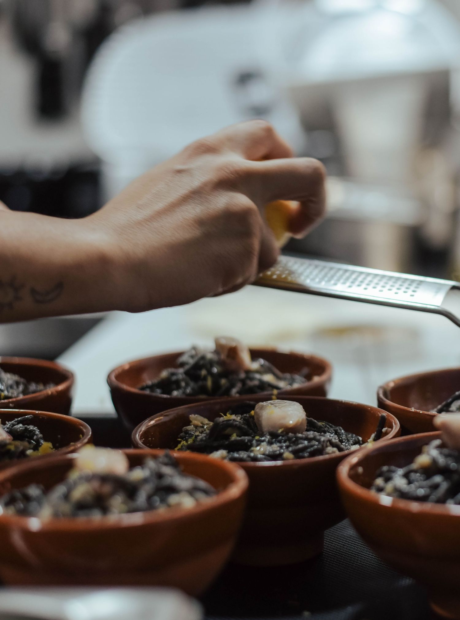 Hands reach for clay bowls filled with dark roasted coffee beans on a rustic wooden surface in soft natural lighting.