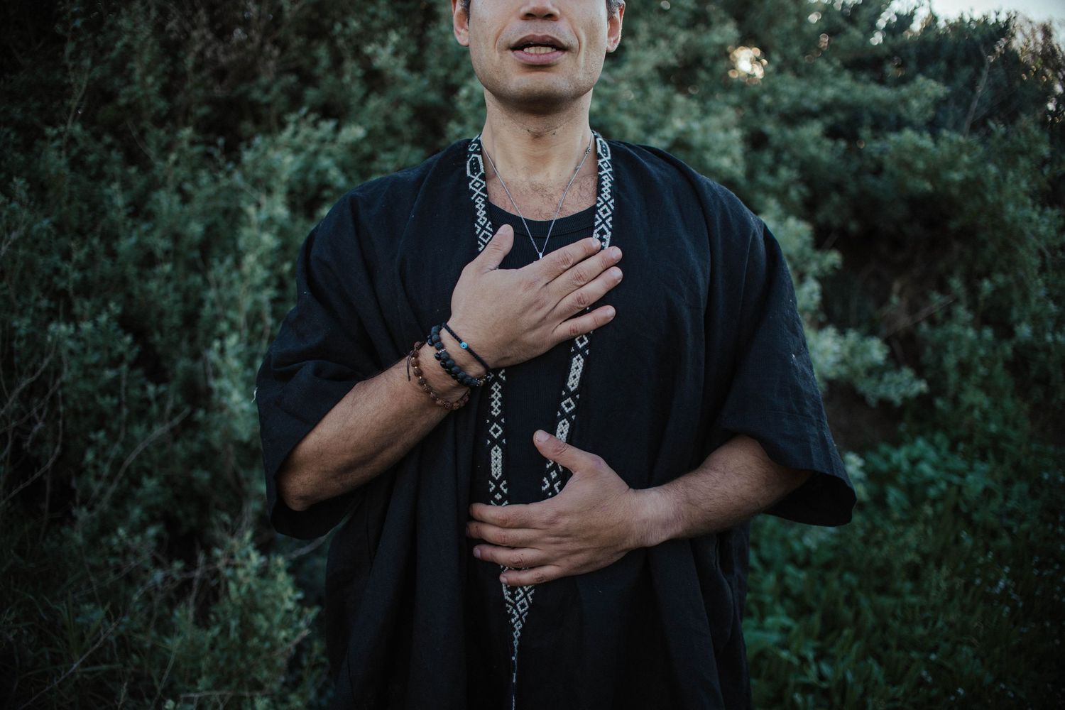 Person in black shirt making expressive gestures against dark green foliage background.