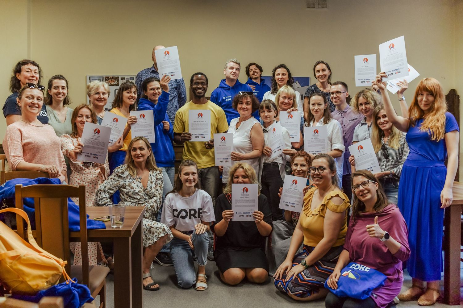 A large group of workshop participants holding up papers and smiling together.