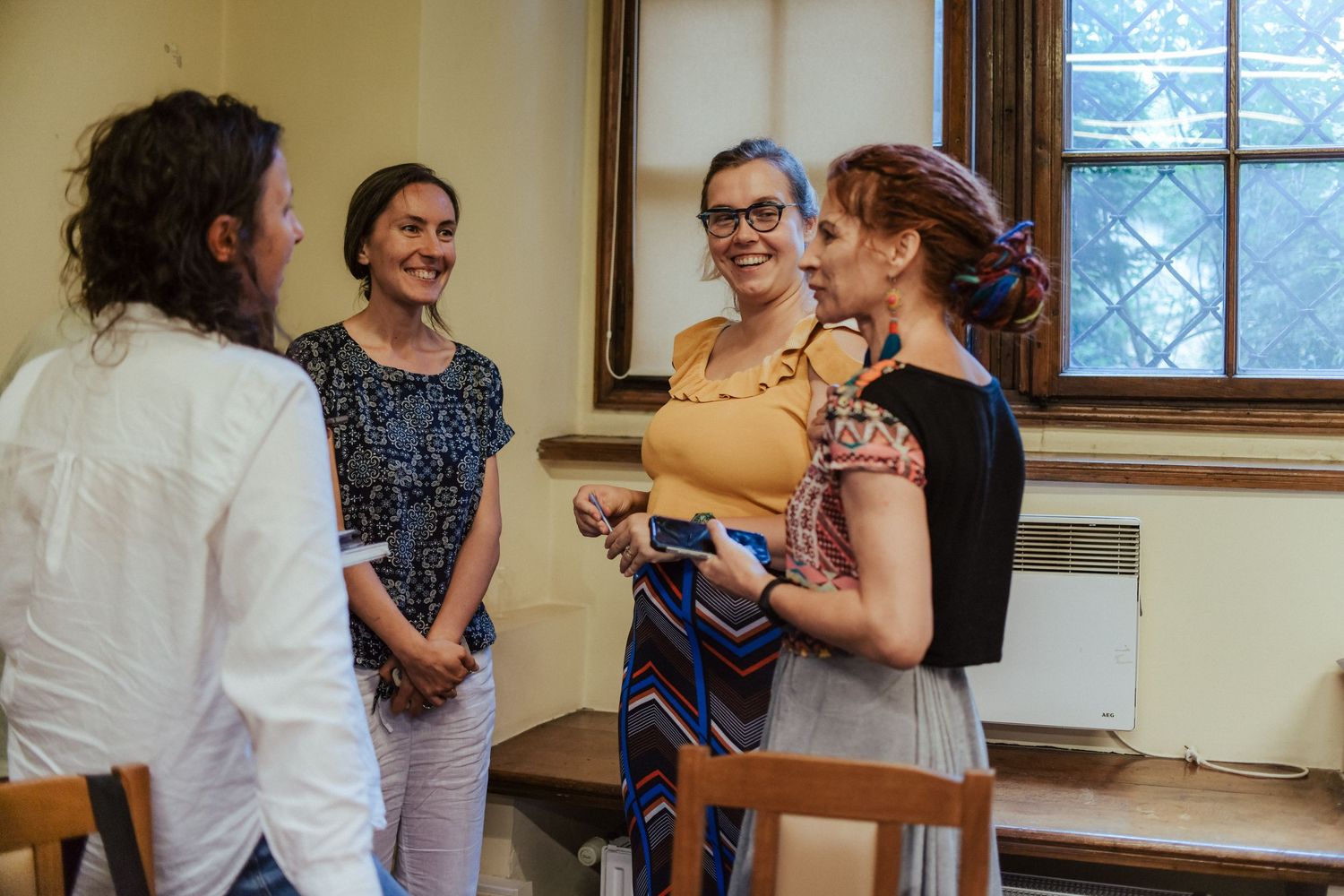 A small group engaged in animated conversation in a room with vintage windows.