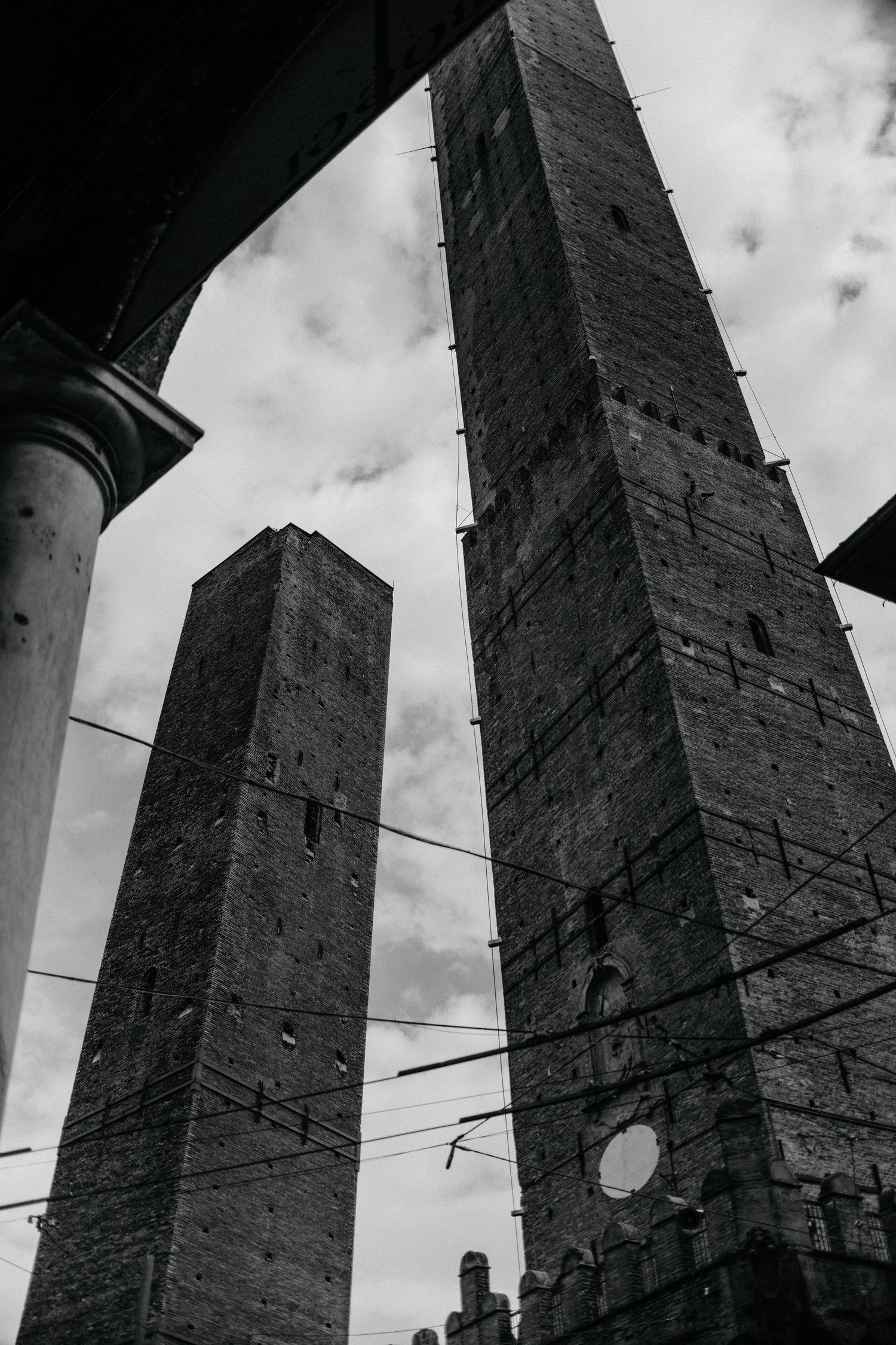 Medieval stone towers of Bologna rise against cloudy sky in dramatic black and white perspective.