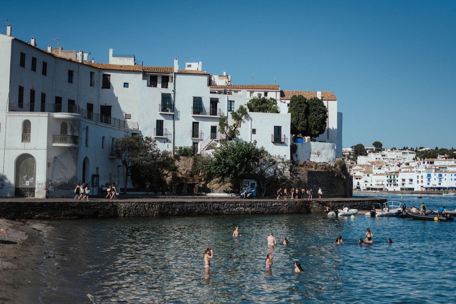 Swimmers enjoy the crystal clear waters near white Mediterranean buildings along the coast of Menorca, Spain.