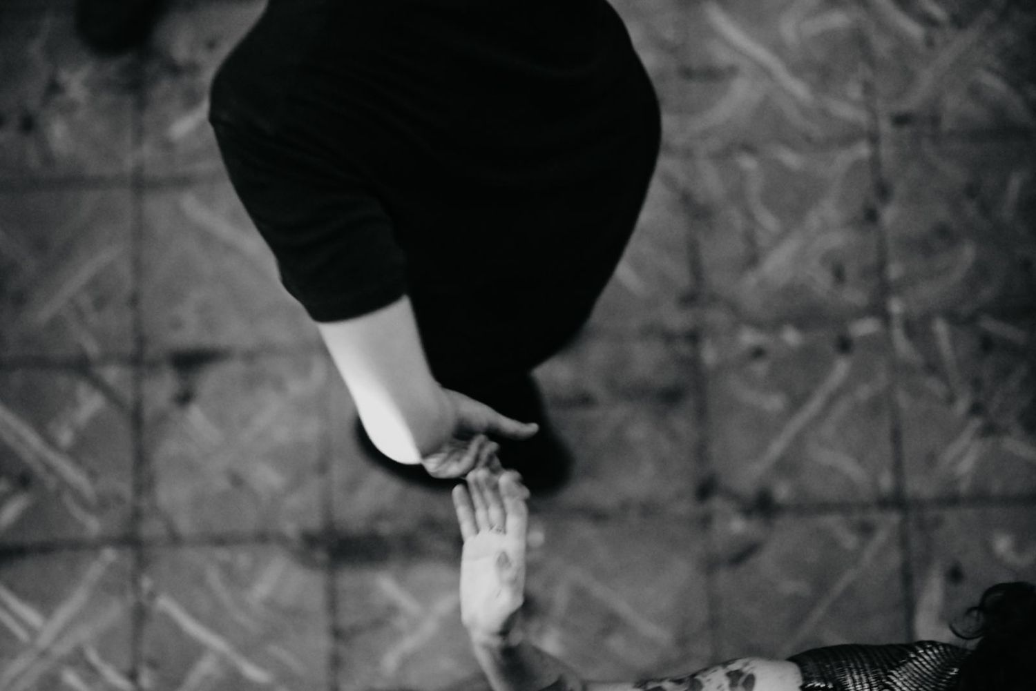 Black and white artistic photograph showing two hands reaching towards each other against a textured background.