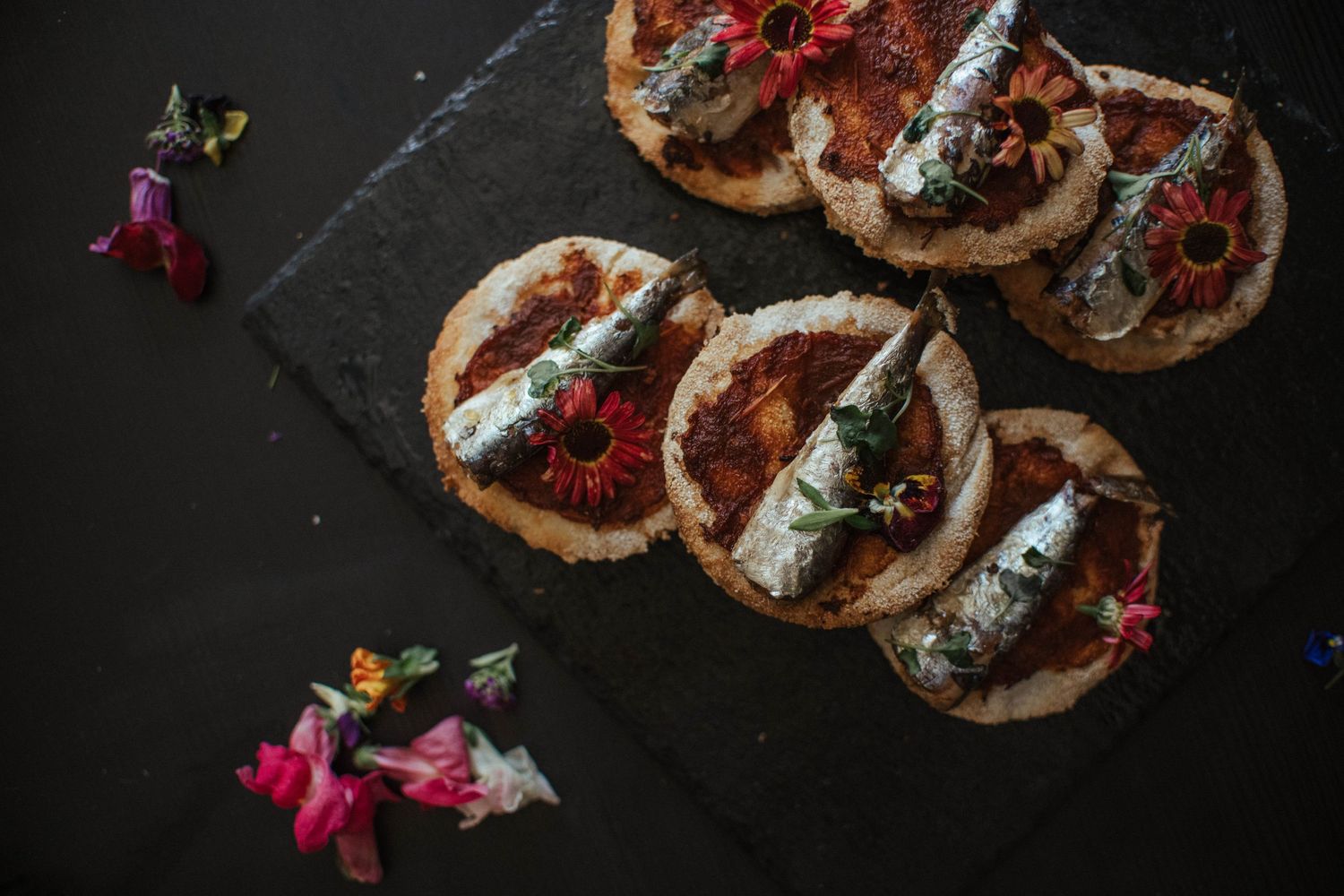 Grilled mushroom and cheese crostini appetizers arranged on a dark slate surface with fresh herbs and garnishes.