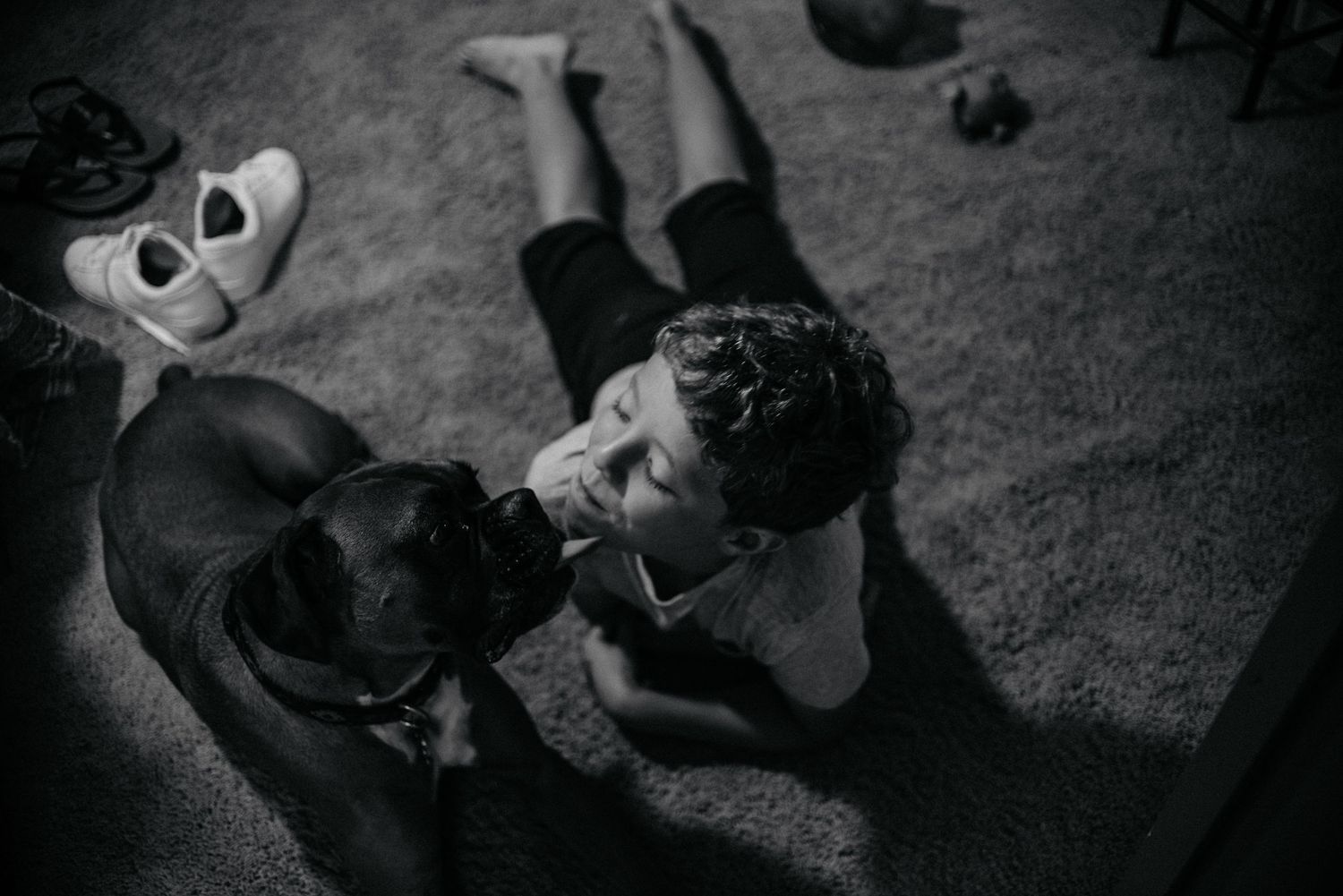A person and dog share a tender moment on the floor in black and white.