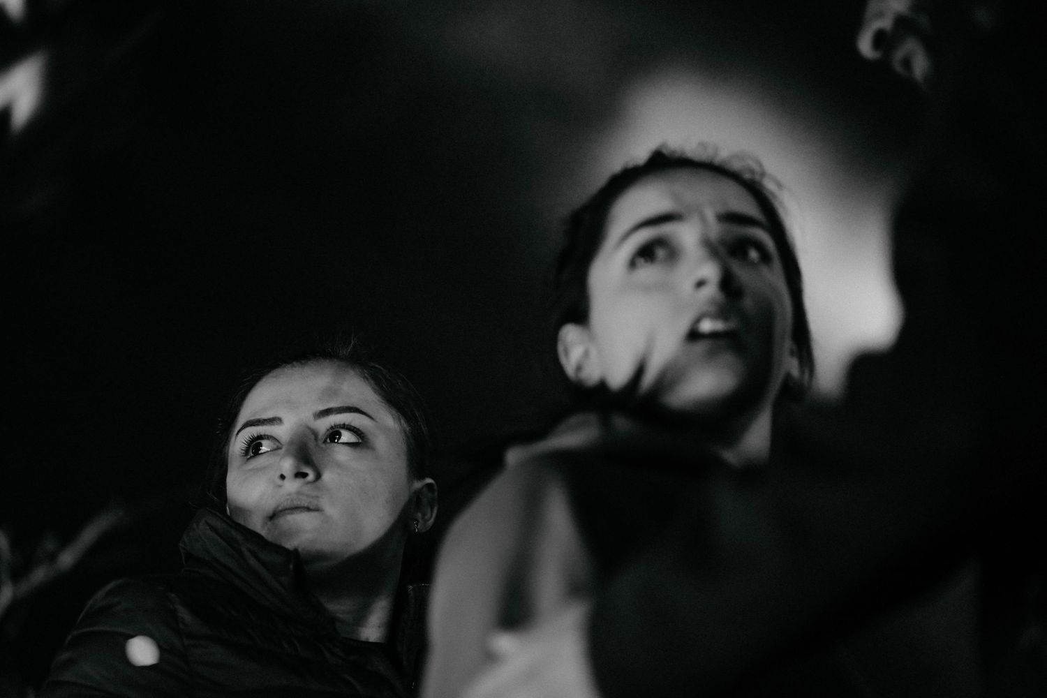 A dramatic black and white photograph shows two figures looking up with intense expressions in dim lighting.