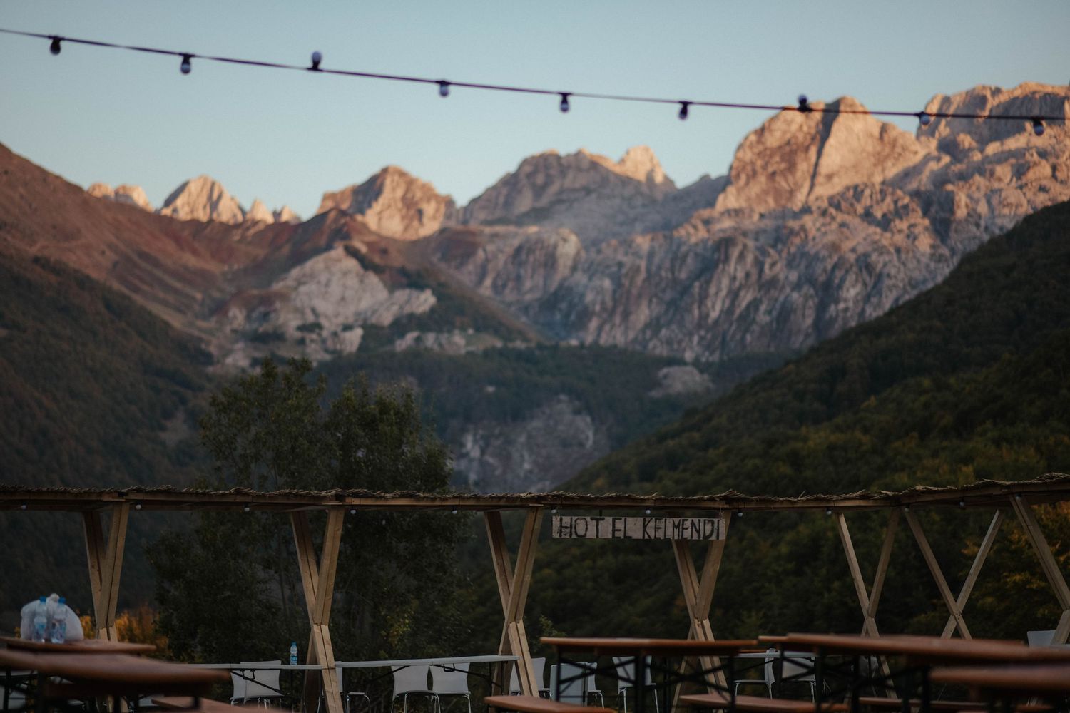 String lights illuminate an outdoor mountain view at sunset with rugged peaks glowing in warm alpenglow light.