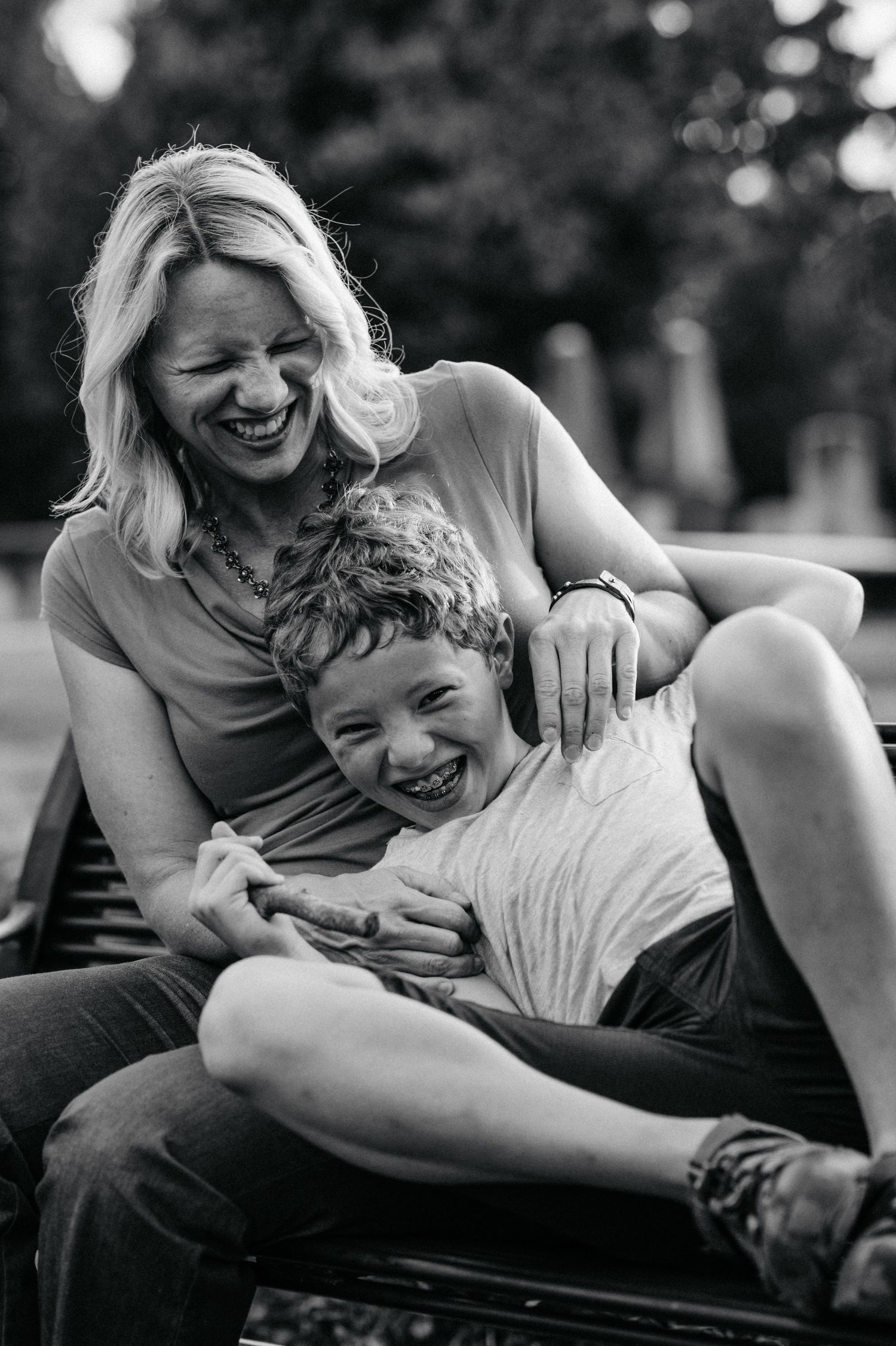 A heartwarming black and white candid photo capturing a joyful moment of laughter and embrace outdoors between mother and son.