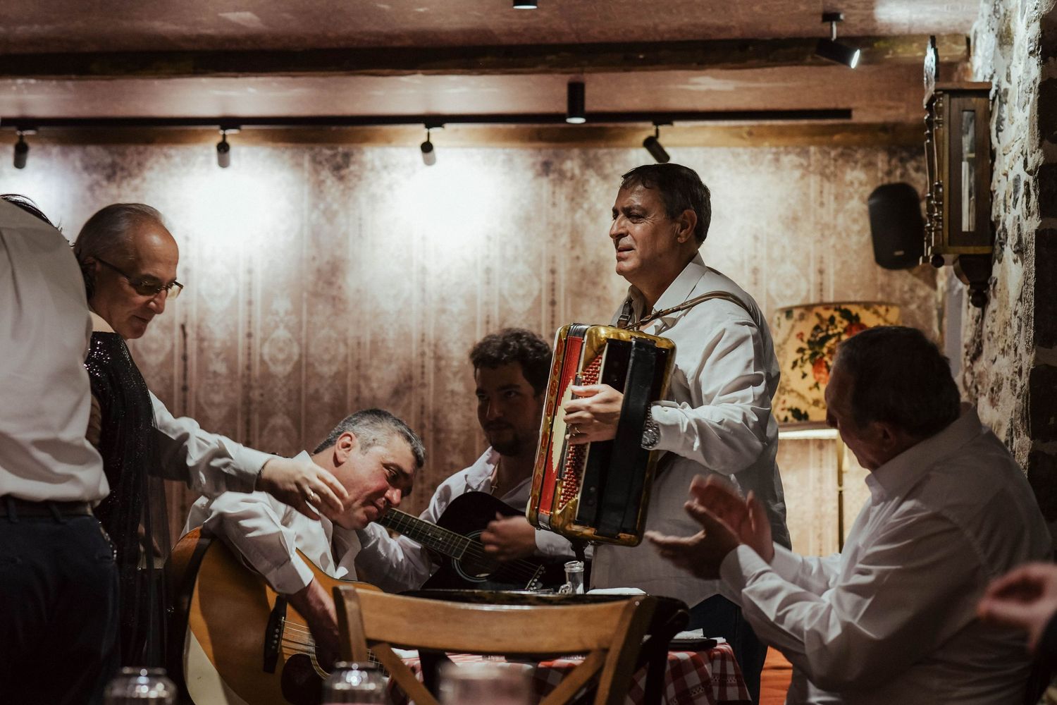 A group gathers around a rustic wooden table in a dimly lit room during what appears to be a meal or meeting.