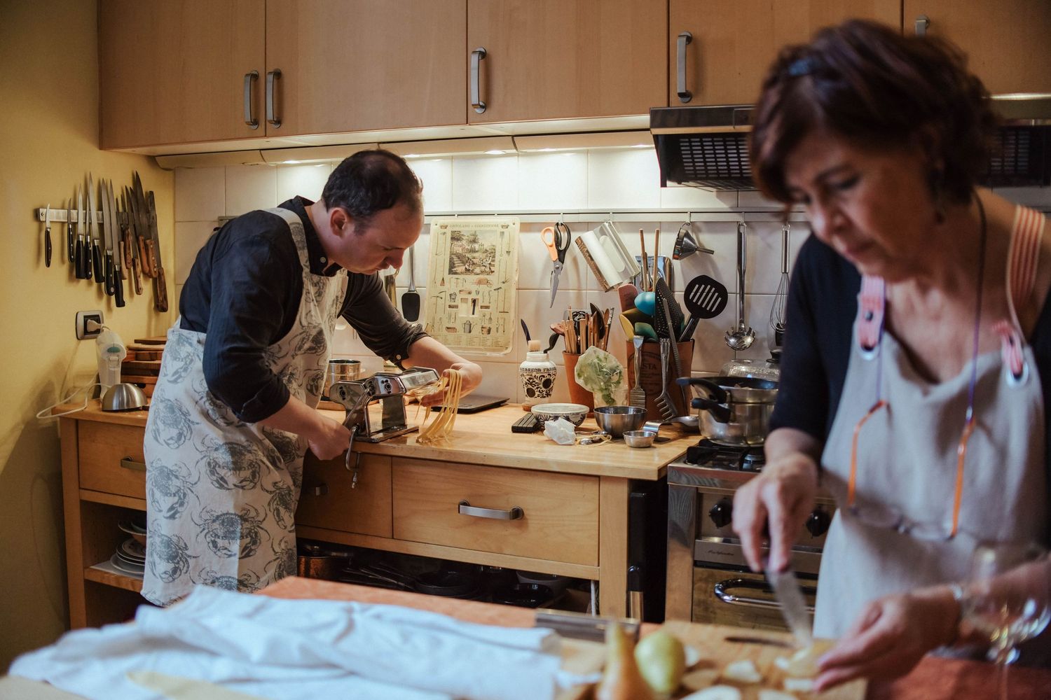 People working at making pasta at wooden tables in an Italian kitchen.