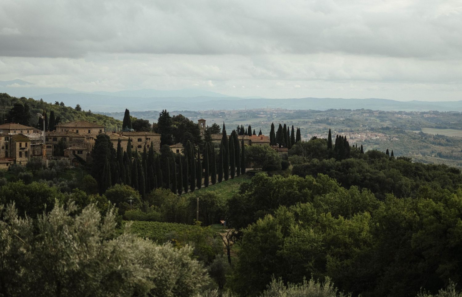 Panoramic view of an Italian villa nestled among cypress trees on a rolling hillside.