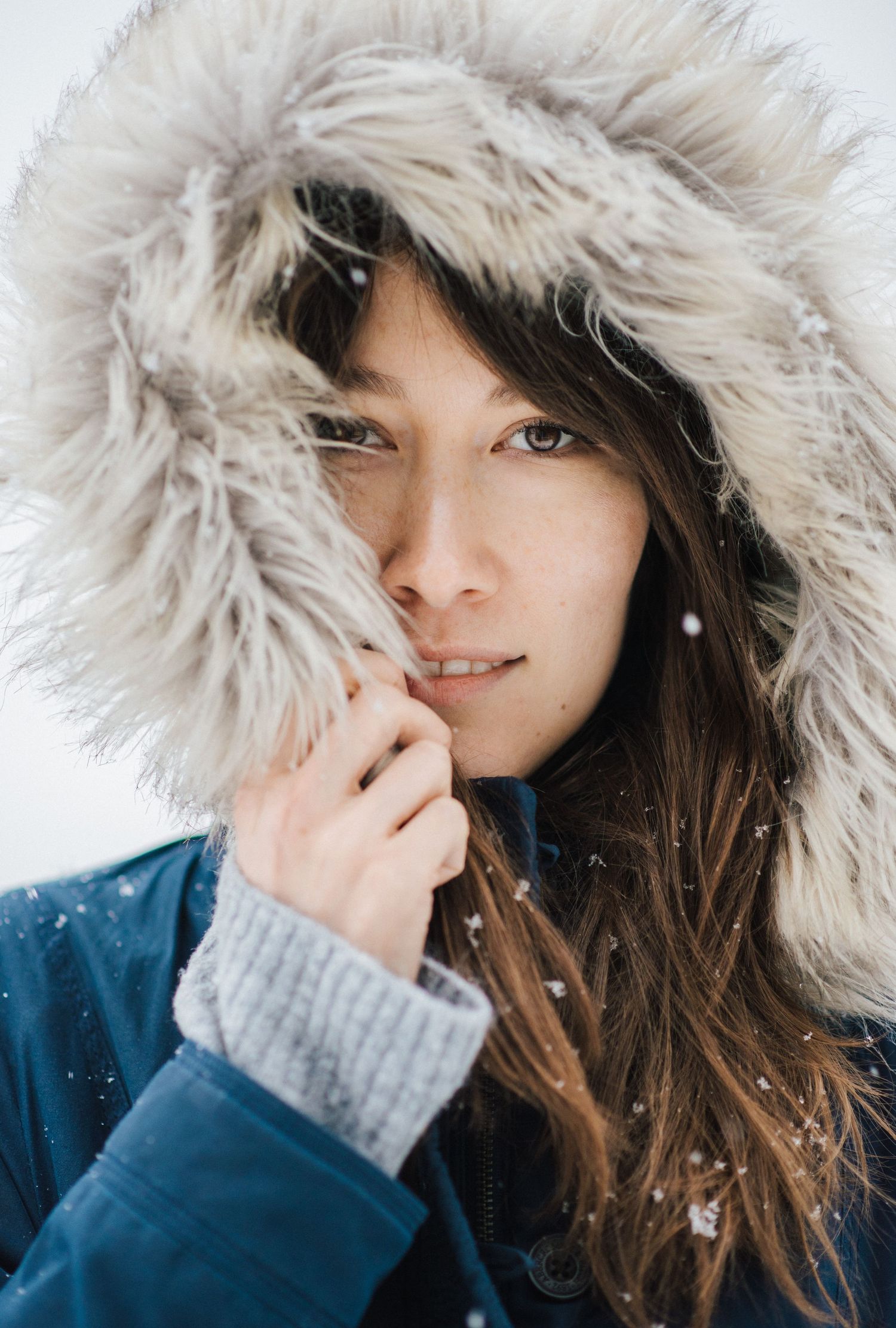 A series of winter portraits showing someone wearing a navy coat with plush fur-trimmed hood in falling snow.