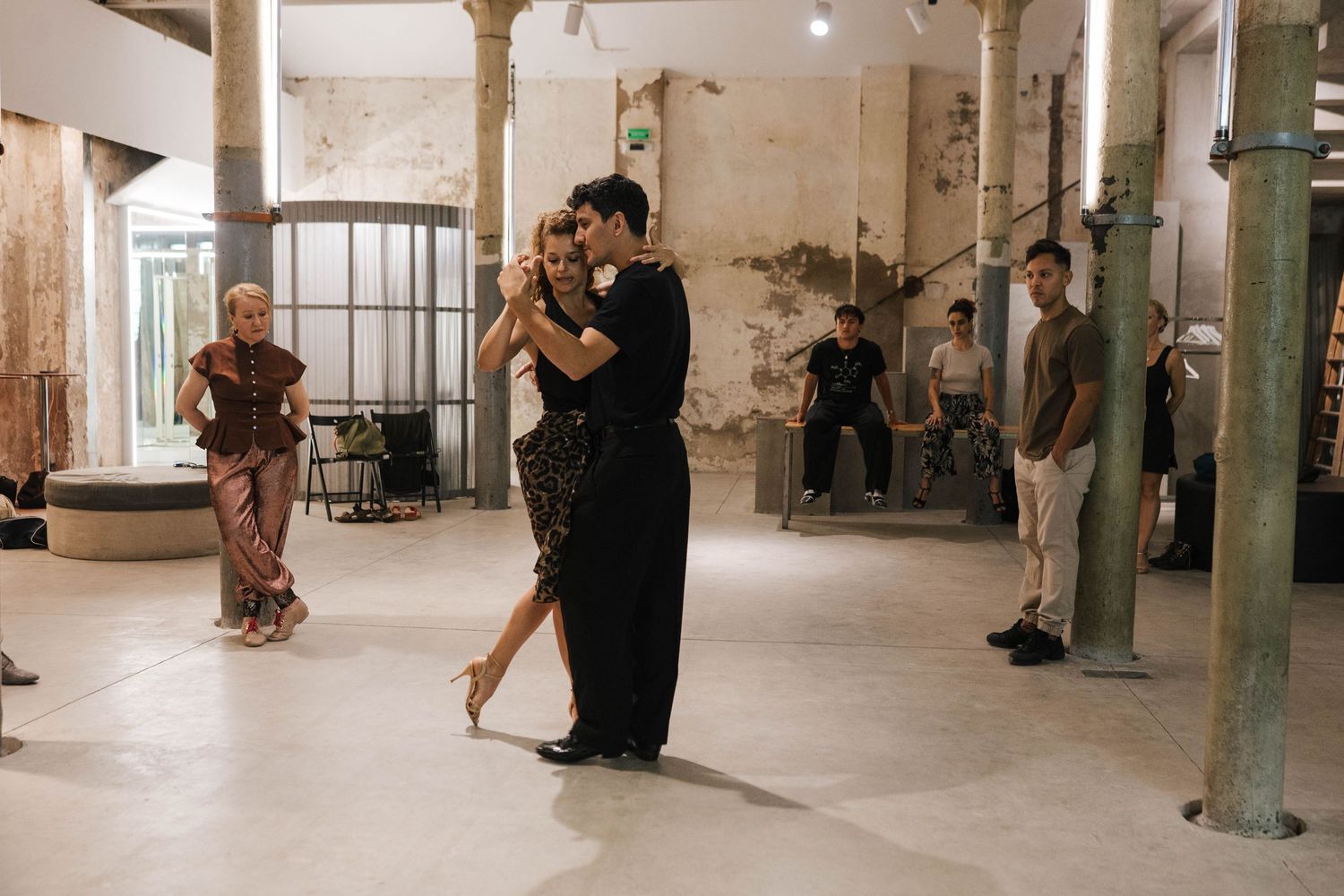 Couple dancing tango in an elegant studio while onlookers watch in the background.