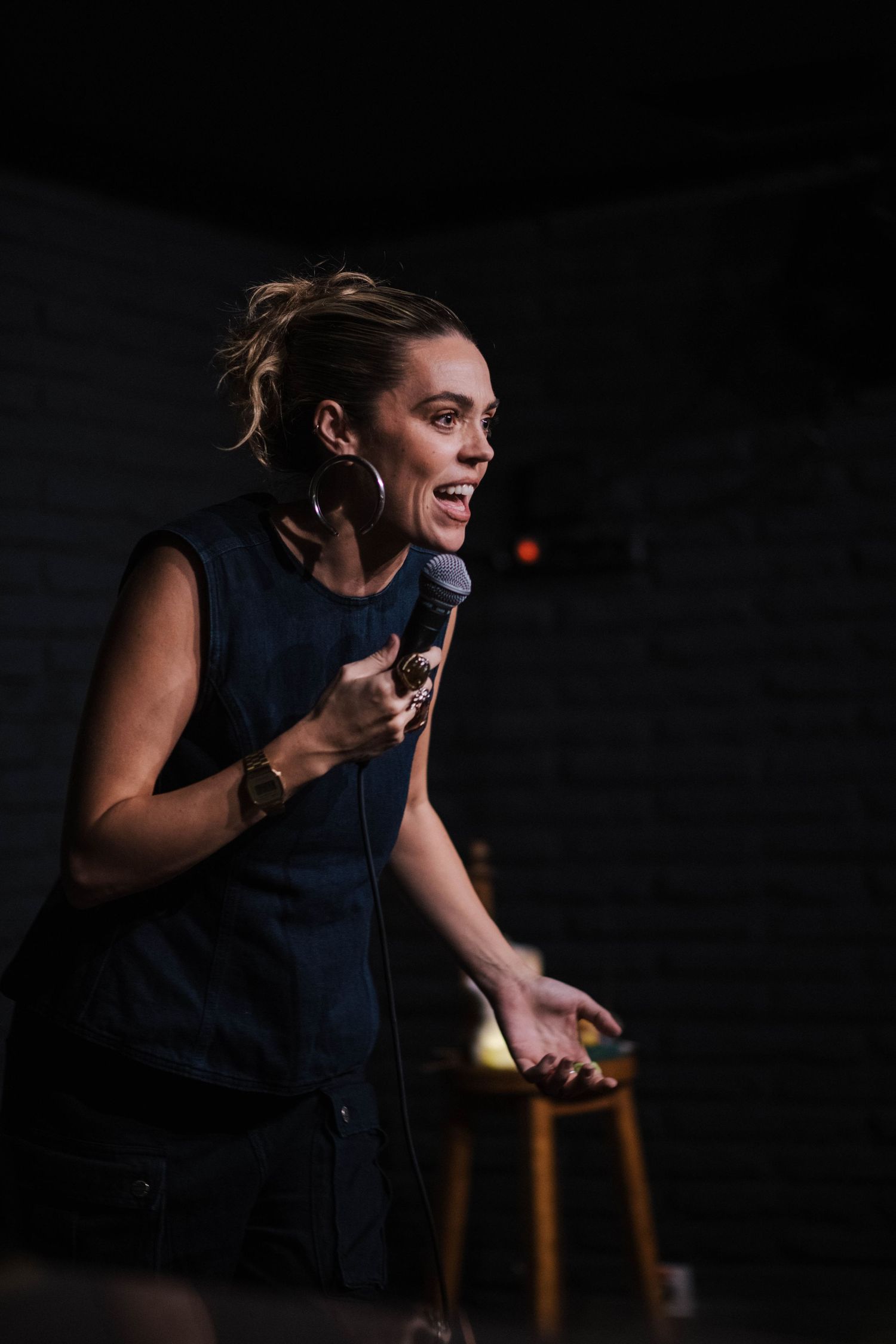 Dramatic side-lit performer gesturing expressively on stage in dark attire.