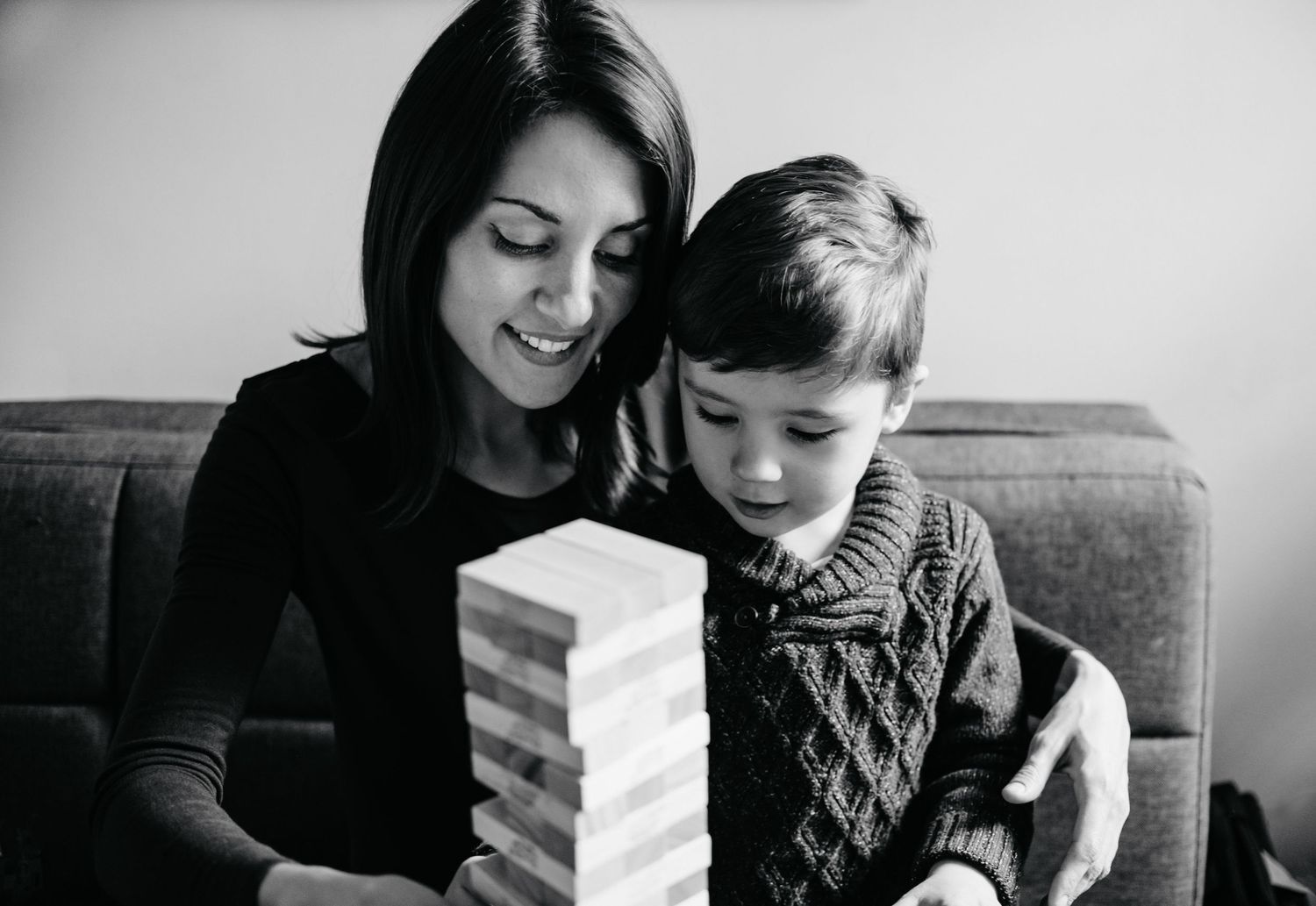 A series of black and white photos showing a parent and child playing Jenga together on a couch.
