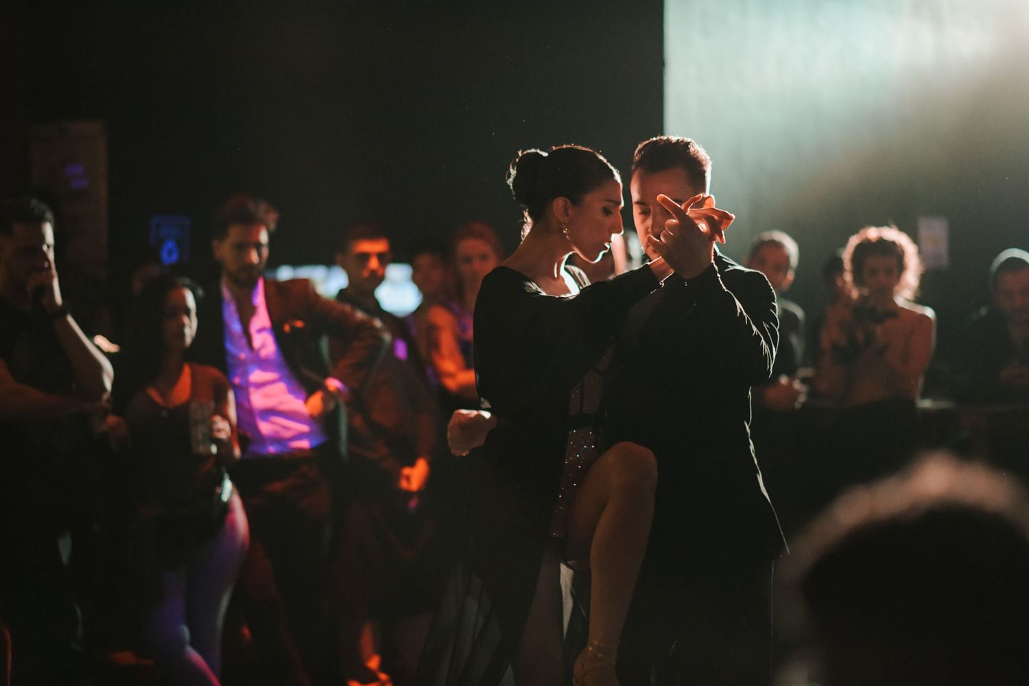 Dance floor scene with atmospheric lighting and dancers creating silhouettes against bright backlighting.