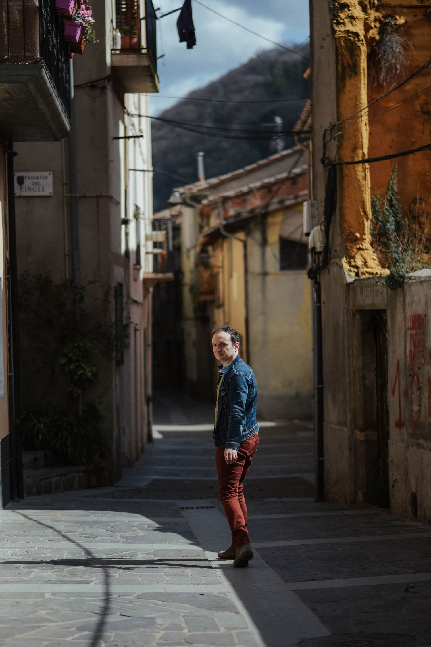 Narrow medieval street with stone buildings and sunlit shadows creating dramatic atmosphere in a Spanish village.