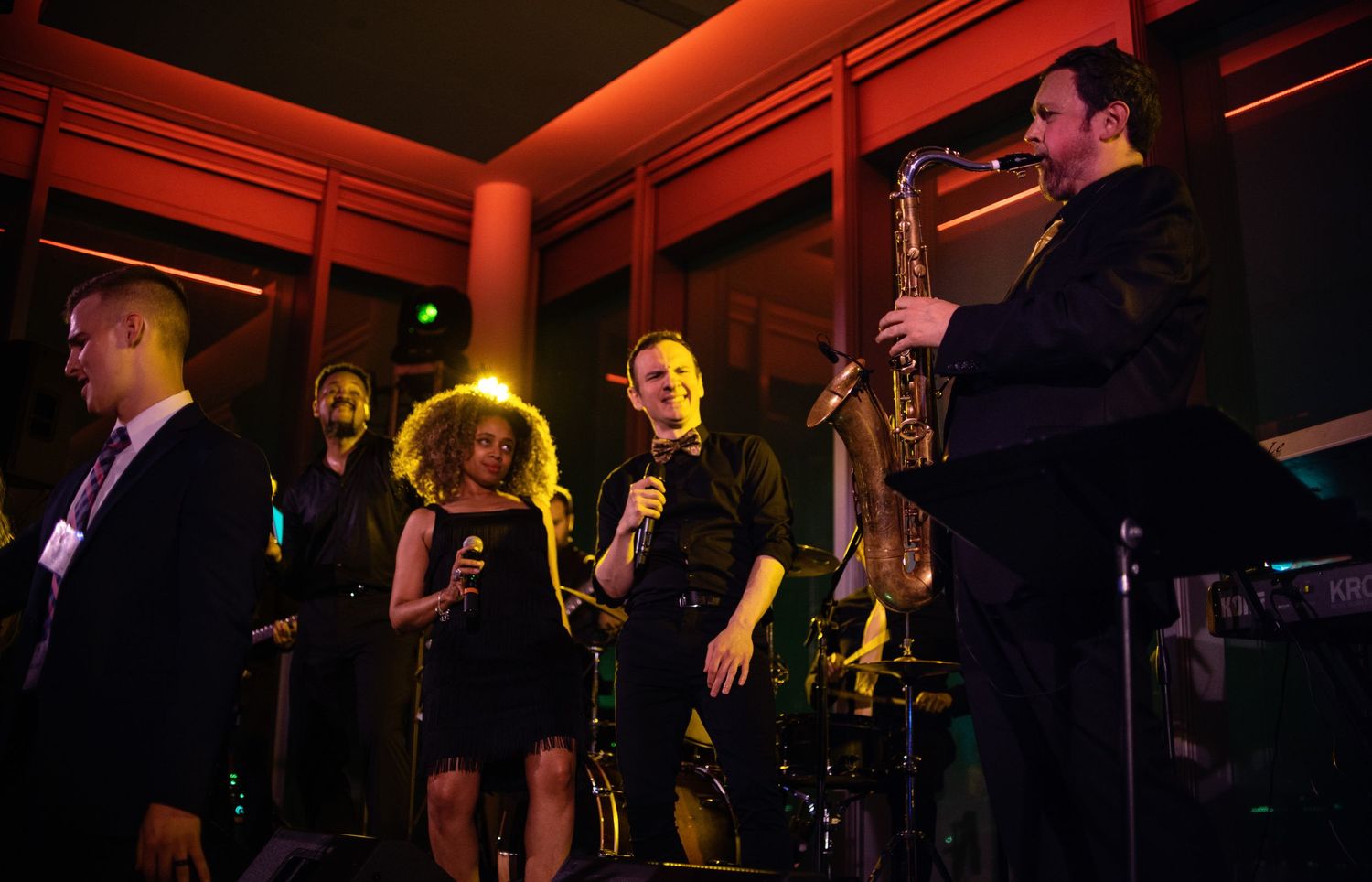 Band members performing on stage with instruments under dramatic orange lighting.