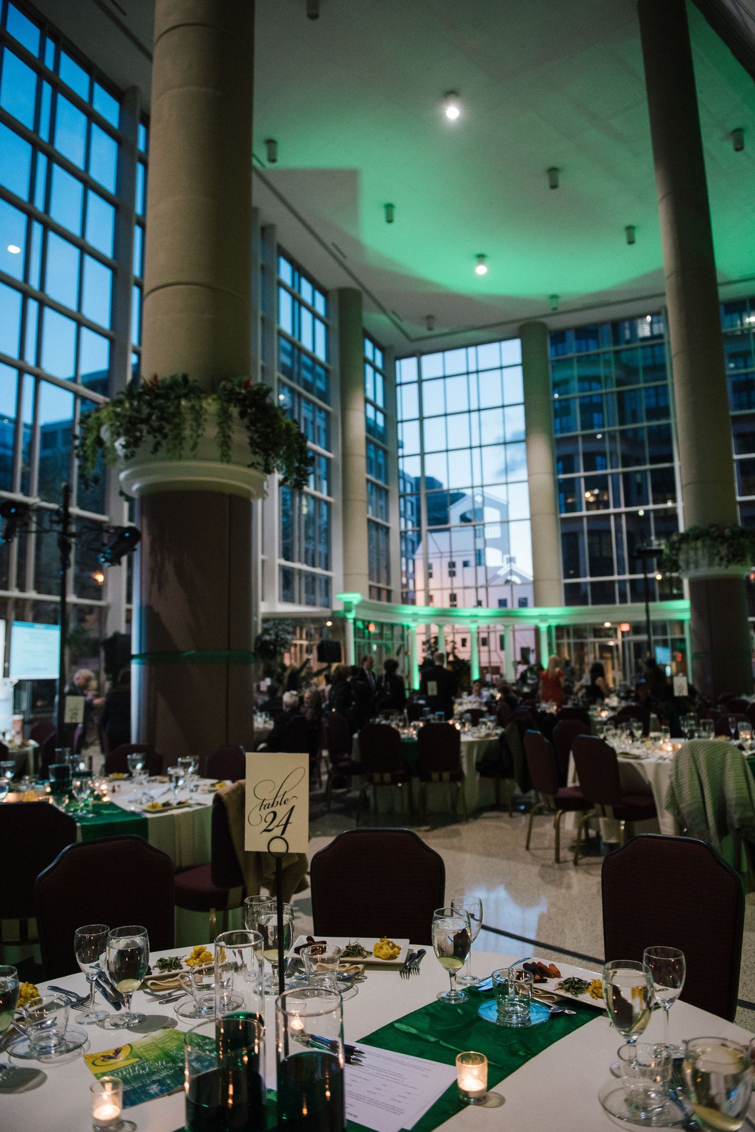 Modern banquet hall with green ambient lighting and elegant table settings for a formal dinner.