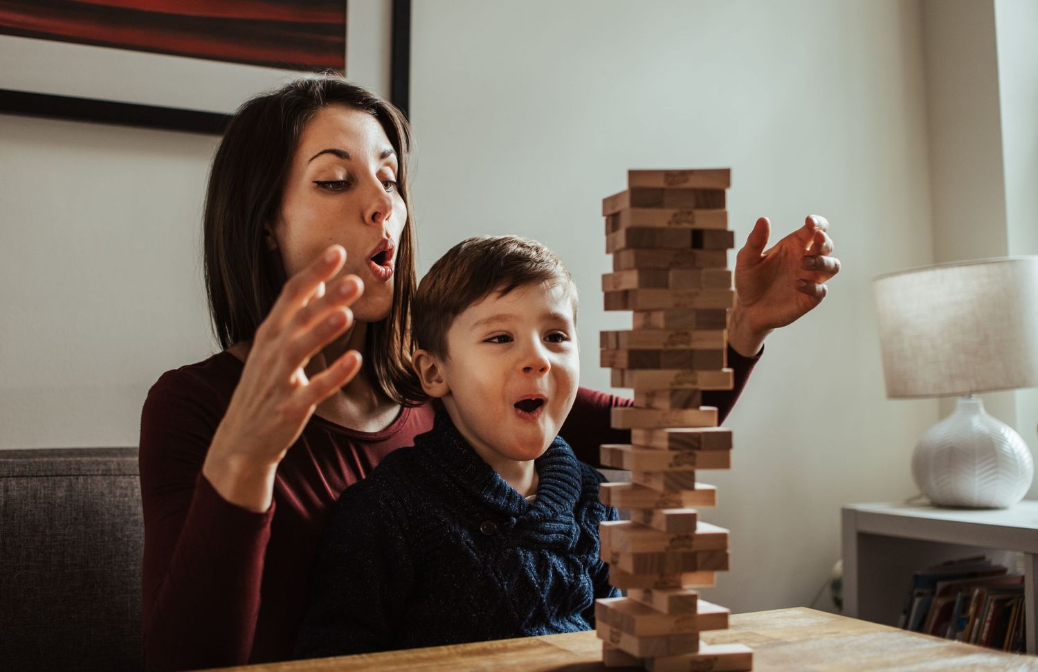 A family plays an intense game of Jenga together at a table, showing expressions of excitement and anticipation.