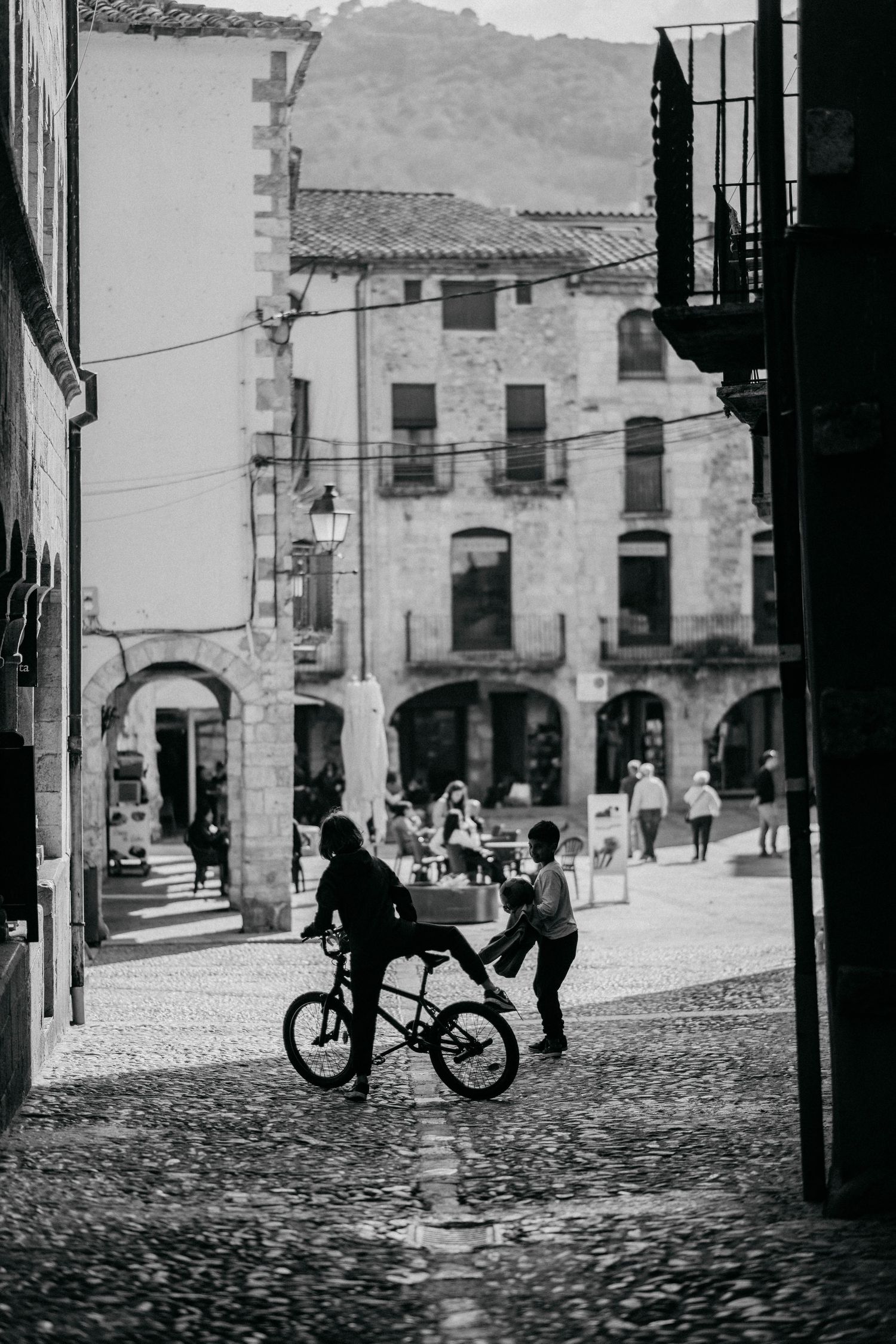 Children playing in a cobblestone plaza surrounded by historic stone buildings in a black and white vintage scene.