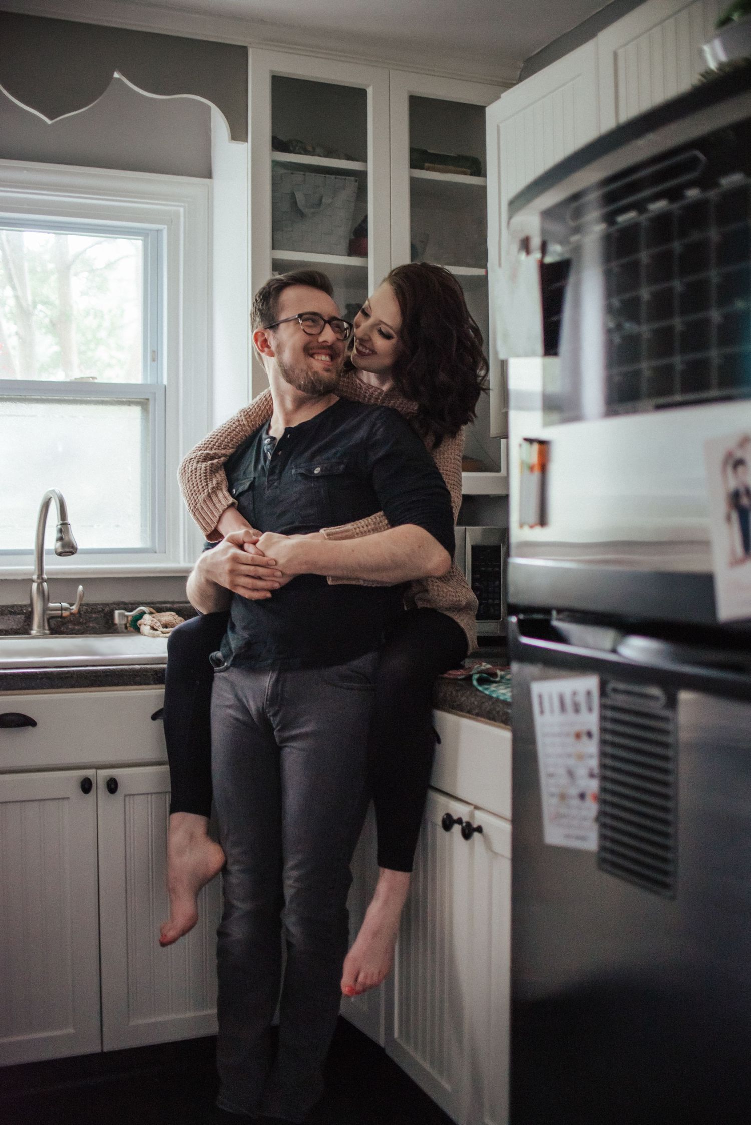 An intimate kitchen moment of a couple captured in soft natural light through window reflections.