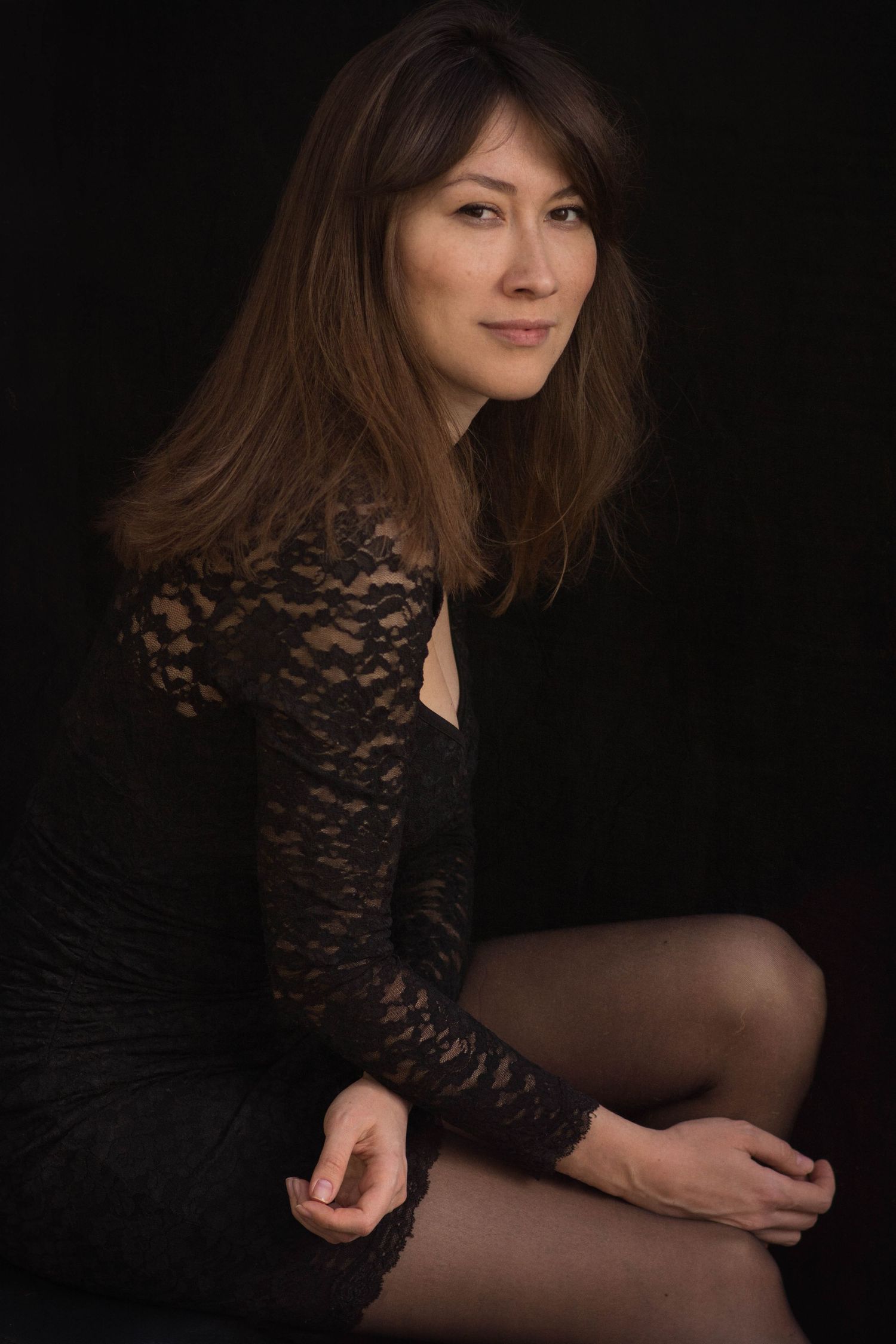 A person in a black lace top poses against a dark background in a series of artistic portrait photographs.