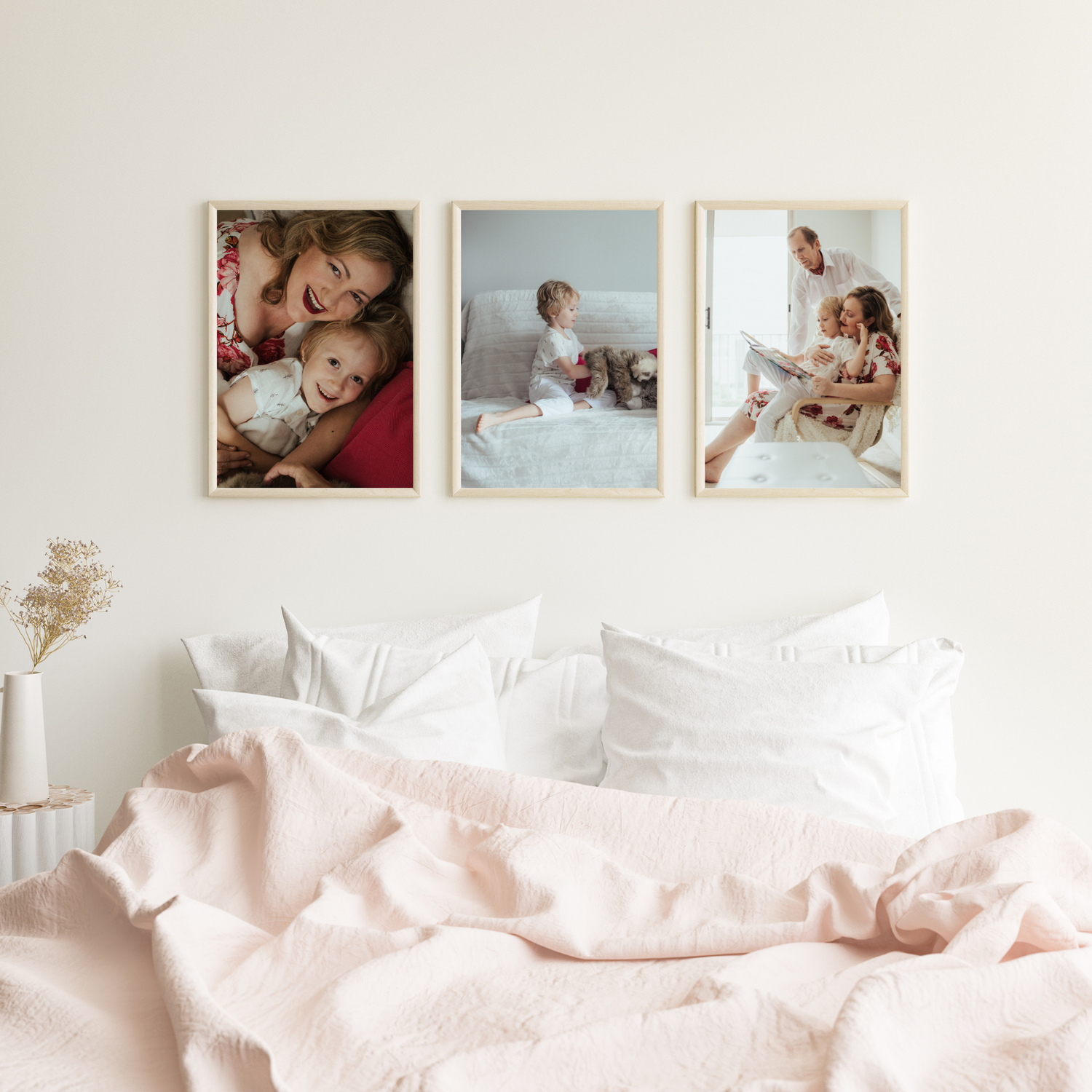 Soft pink bedding and pillows arranged on a white bed with framed photos on the wall above.