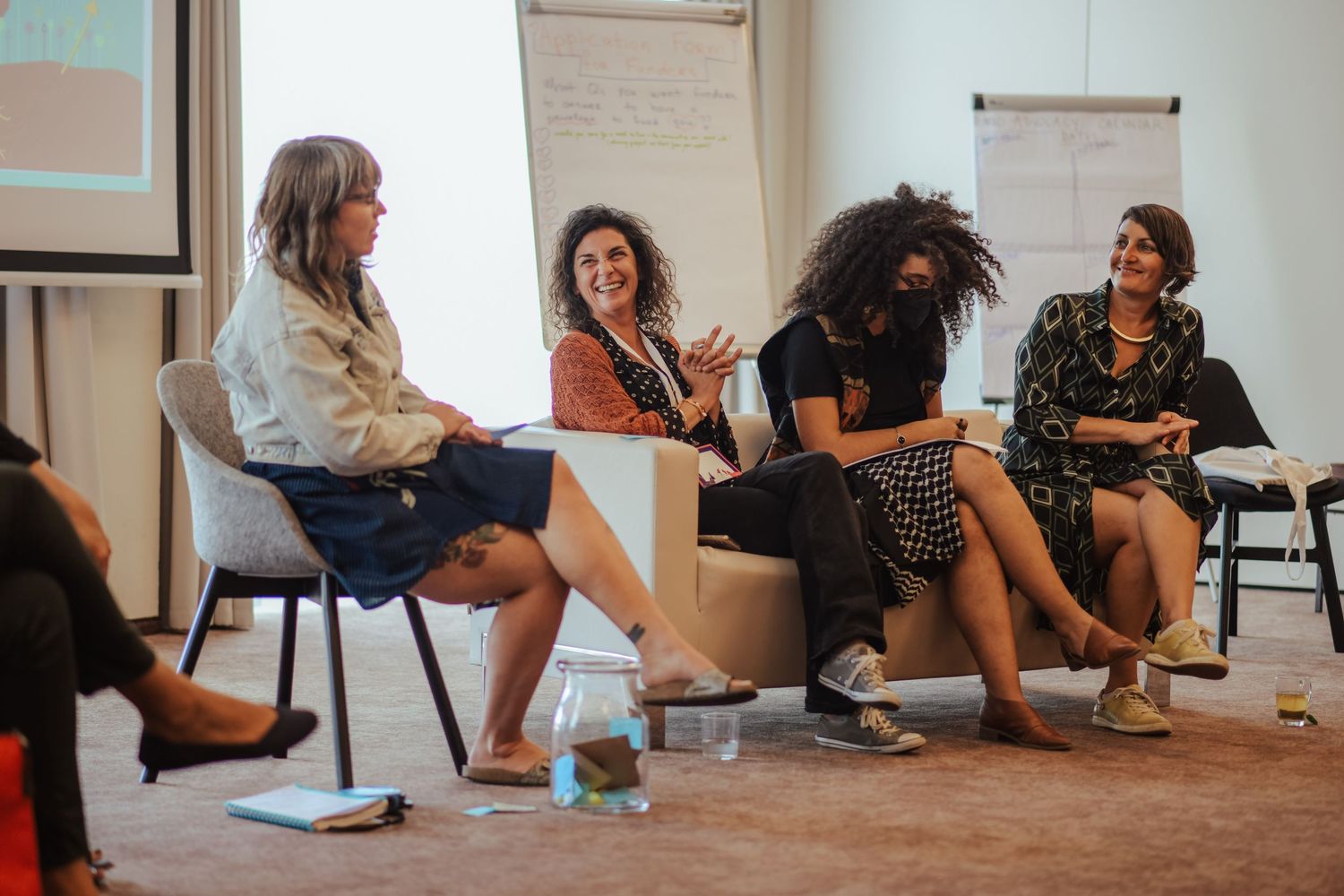 Group discussion in a casual office setting with natural lighting and presentation materials.