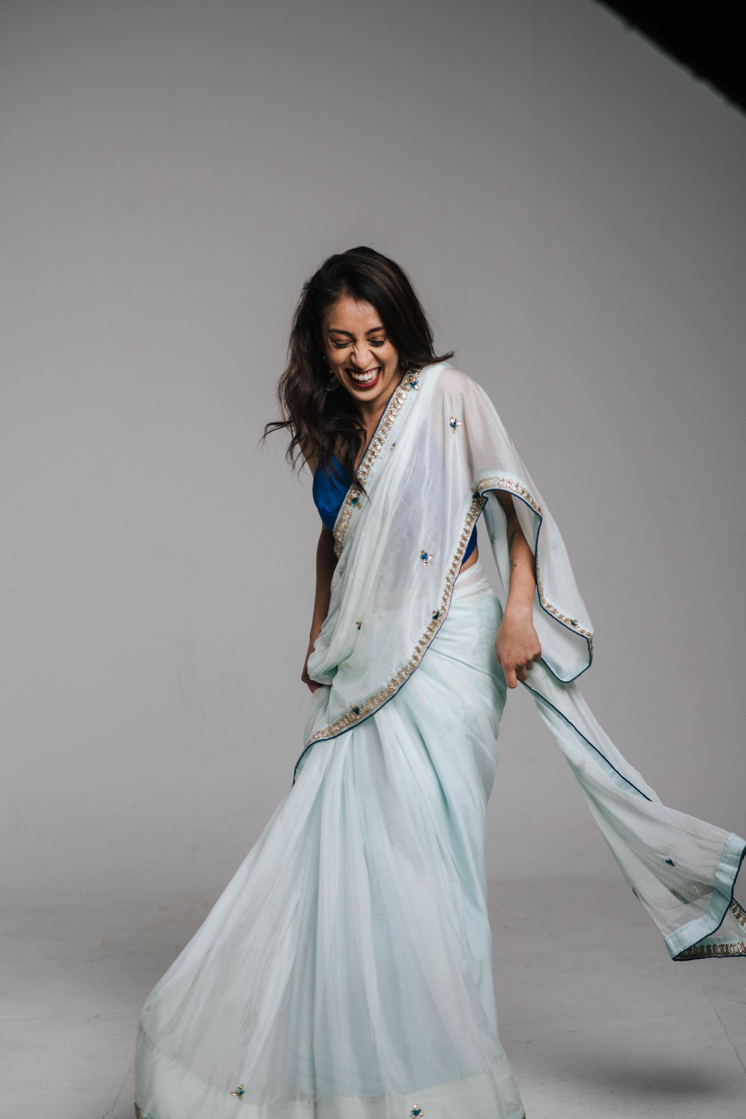 A person in a flowy white dress spins and dances joyfully against a gray studio backdrop.